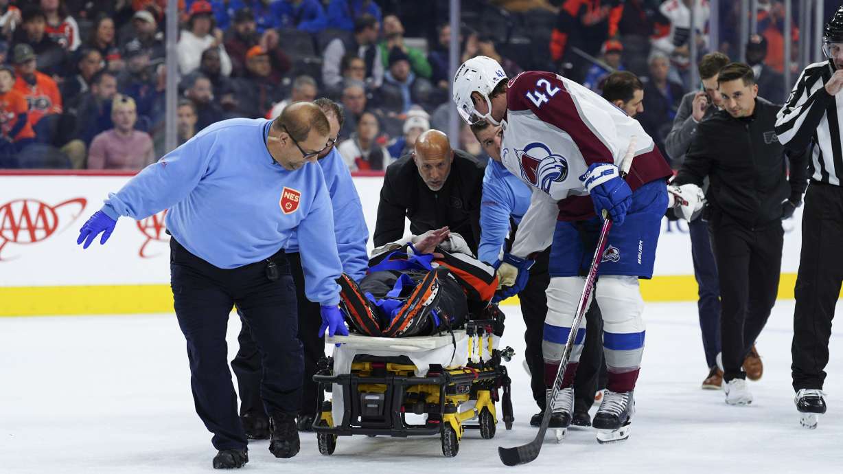 Colorado Avalanche's Josh Manson (42), right, talks to referee Mitch Dunning, center, as Dunning is stretchered off the ice after an injury during the first period of an NHL hockey game between the Philadelphia Flyers and the Avalanche, Monday, Nov. 18, 2024, in Philadelphia.