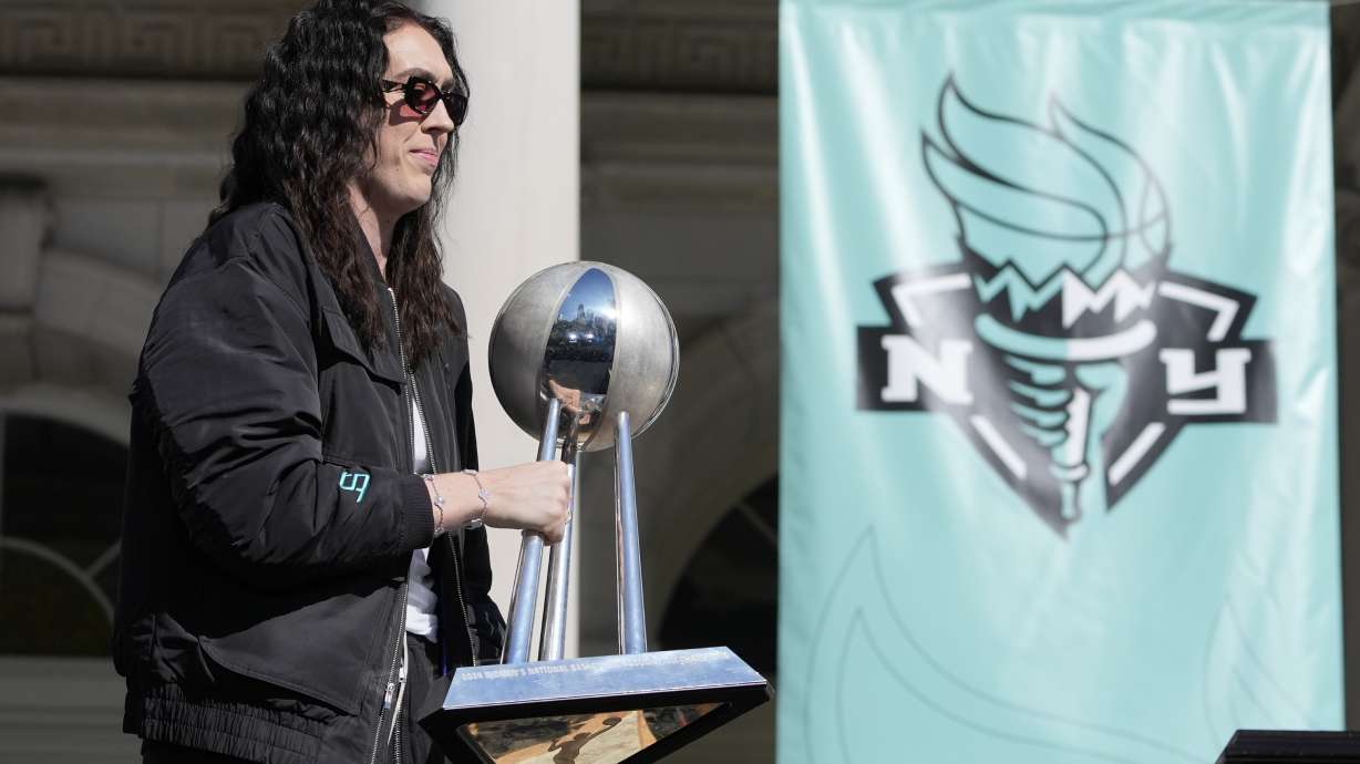 New York Liberty Breanna Stewart places the championship trophy on a table as she arrives on stage during a ceremony after a parade in honor of the Liberty's WNBA basketball championship at City Hall in New York, Thursday, Oct. 24, 2024.