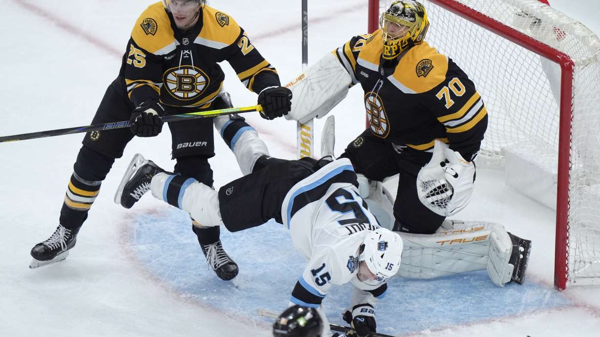 Utah Hockey Club center Alexander Kerfoot (15) tumbles in front of Boston Bruins defenseman Brandon Carlo (25) and goaltender Joonas Korpisalo (70) in the second period of an NHL hockey game, Thursday, Nov. 21, 2024, in Boston.