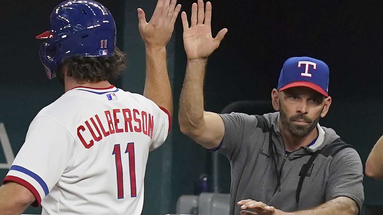 FILE - Texas Rangers' Charlie Culberson (11) gets a high five from manager Chris Woodward after scored on a sacrifice bunt by teammate Bubba Thompson during the fourth inning of a baseball game against the Seattle Mariners in Arlington, Texas, on Aug. 13, 2022.