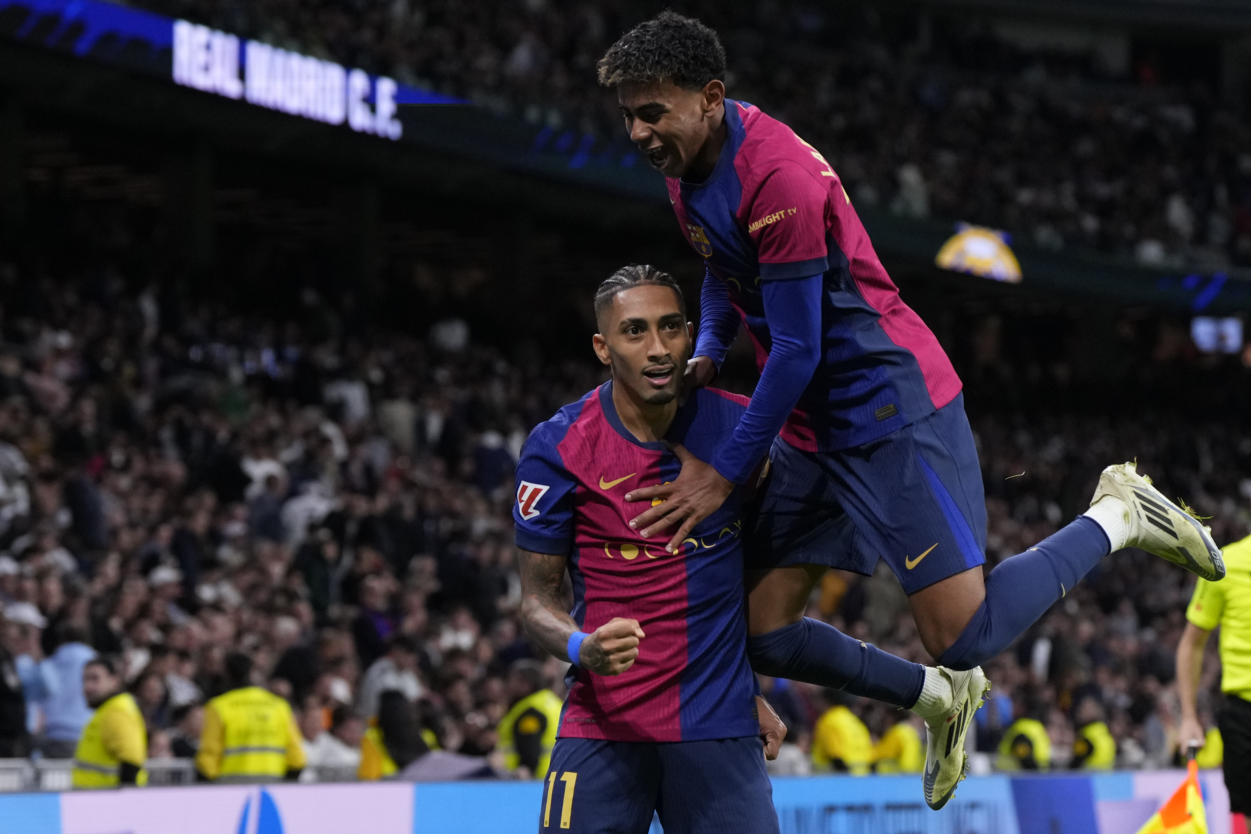 Barcelona's Raphinha celebrates with Barcelona's Lamine Yamal, top, after scoring his side's fourth goal during a Spanish La Liga soccer match between Real Madrid and Barcelona at the Santiago Bernabeu stadium in Madrid, Spain, Saturday, Oct. 26, 2024. 