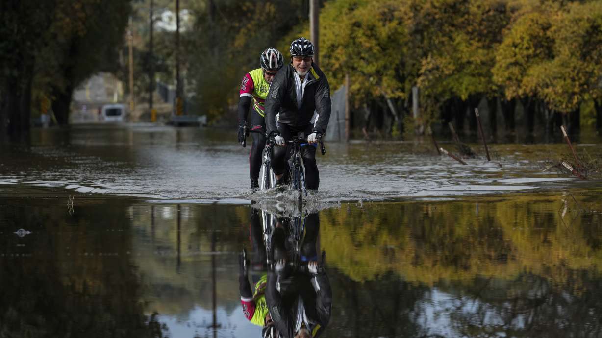 Dave Edmonds, right, and Mike Raasch ride their bicycles on a flooded road Saturday, in Windsor, Calif. The U.S. is reeling from snow and rain while preparing for another bout of bad weather.