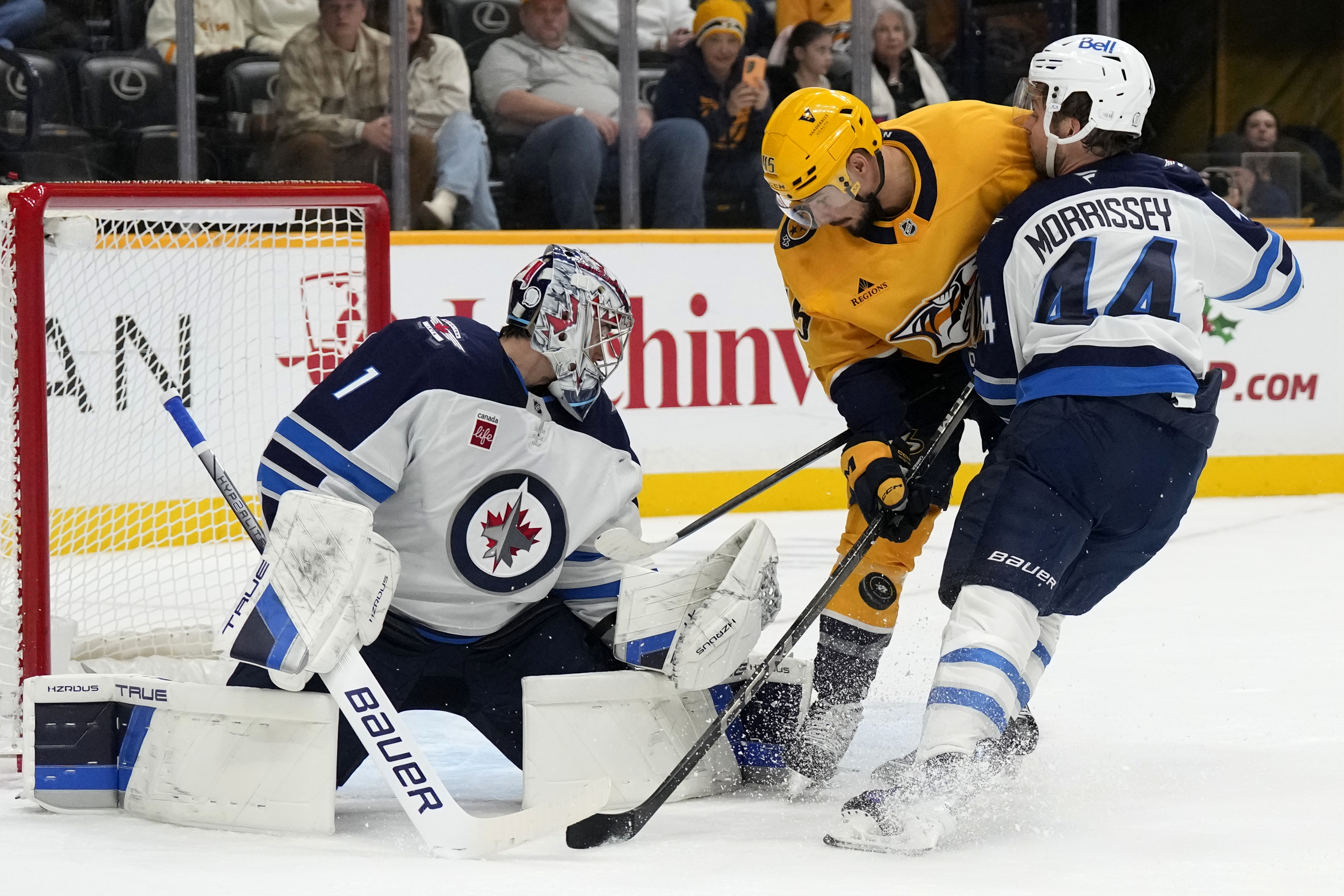 Winnipeg Jets goaltender Eric Comrie (1) reaches for a shot as Jets' Josh Morrissey (44) and Nashville Predators' Alexandre Carrier (45) battle in front of the net during the second period of an NHL hockey game Saturday, Nov. 23, 2024, in Nashville, Tenn.