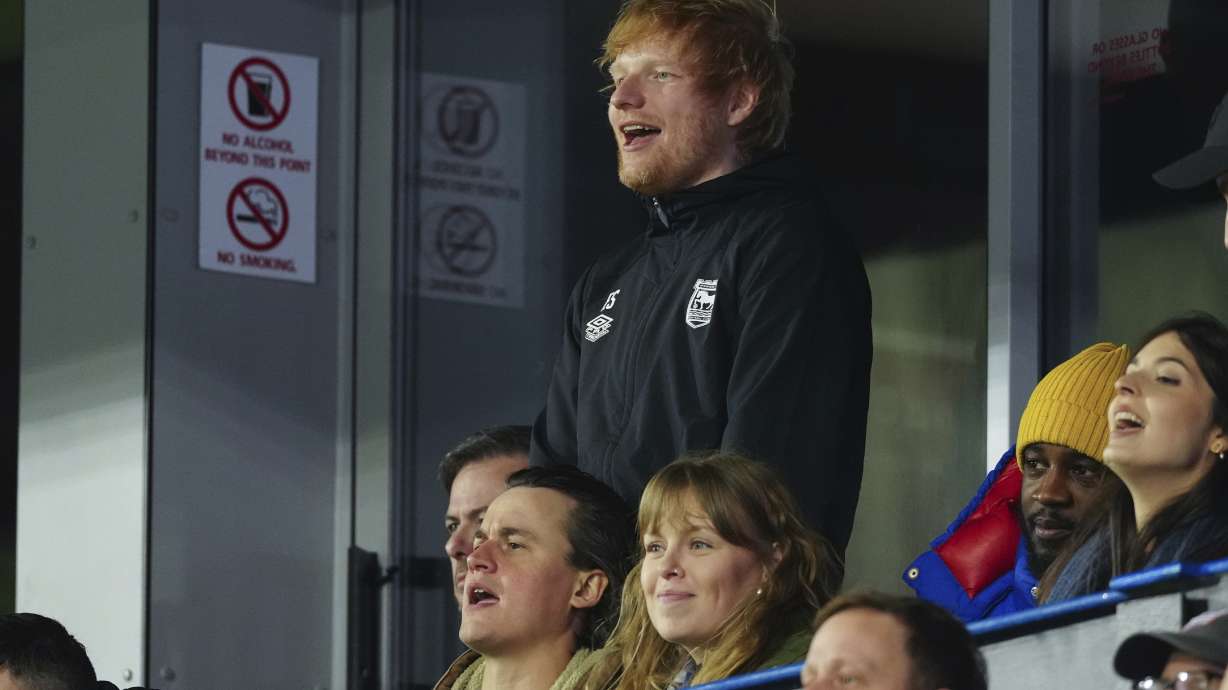 Ipswich Town fan Ed Sheeran, top, cheers for his team during the English Premier League soccer match between Ipswich Town and Manchester United at Portman Road stadium in Ipswich, England, Sunday, Nov. 24, 2024.