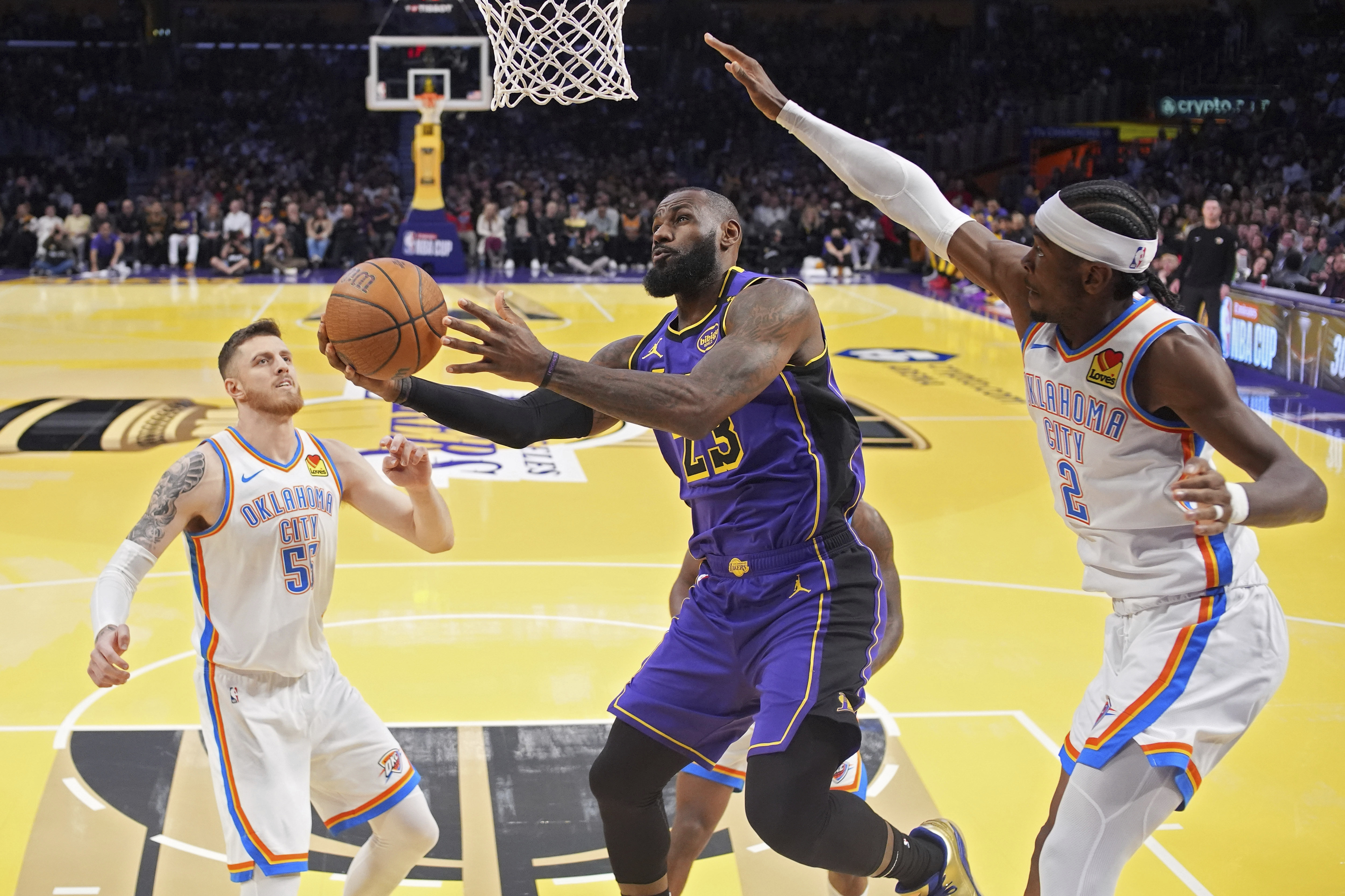 Los Angeles Lakers forward LeBron James, center, shoots as Oklahoma City Thunder center Isaiah Hartenstein, left, and guard Shai Gilgeous-Alexander defend during the first half of an Emirates NBA Cup basketball game, Friday, Nov. 29, 2024, in Los Angeles. 