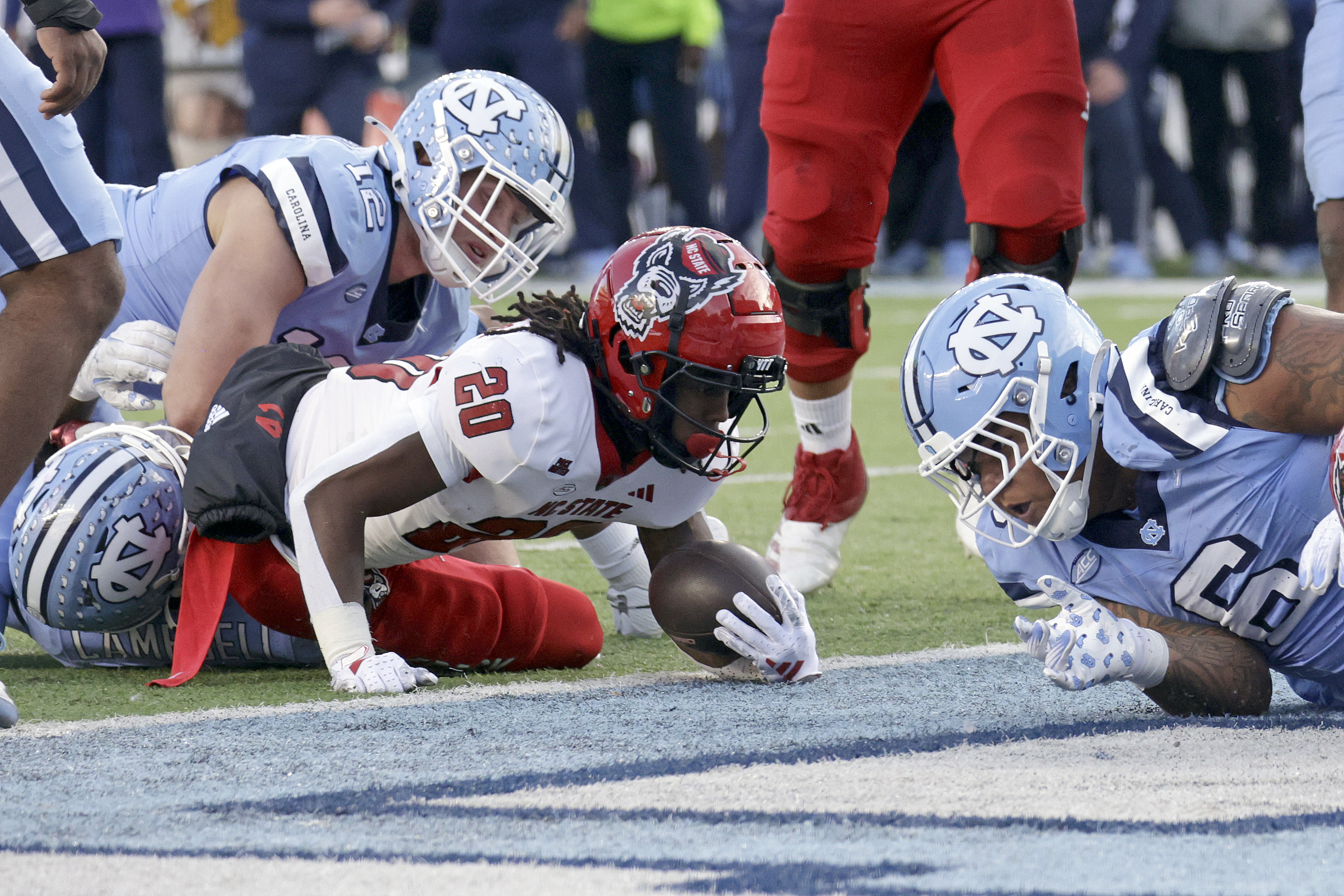 North Carolina State running back Hollywood Smothers (20) gets into the end zone for a touchdown as he's defended by North Carolina defensive linemen Beau Atkinson (12) and Joshua Harris (6) during the first half of an NCAA college football game Saturday, Nov. 30, 2024, in Chapel Hill, N.C. 