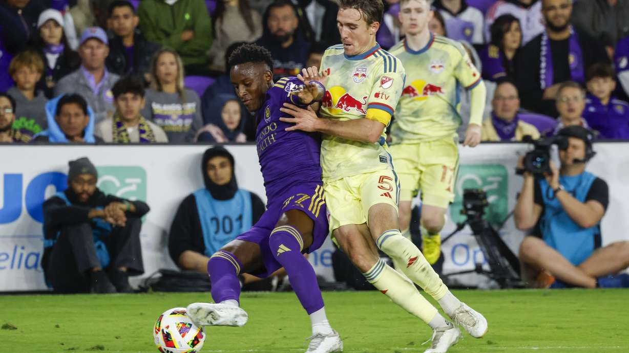 Orlando City forward Iván Angulo, left, is defended New York Red Bulls midfielder Peter Stroud, middle, and forward Cameron Harper, right, during the first half of an MLS Eastern Conference final soccer match, Saturday, Nov. 30, 2024, in Orlando, Fla.