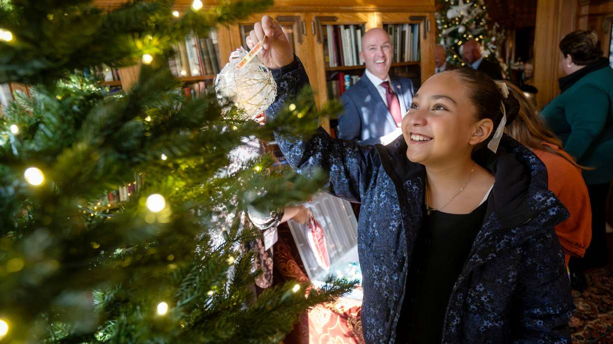 Kiera Esquibel hangs an ornament on the tree as Gov. Spencer Cox and first lady Abby Cox welcome kids from Polk Elementary in Ogden into the Governor's Mansion in Salt Lake City on Monday to decorate a Christmas tree and mantel.