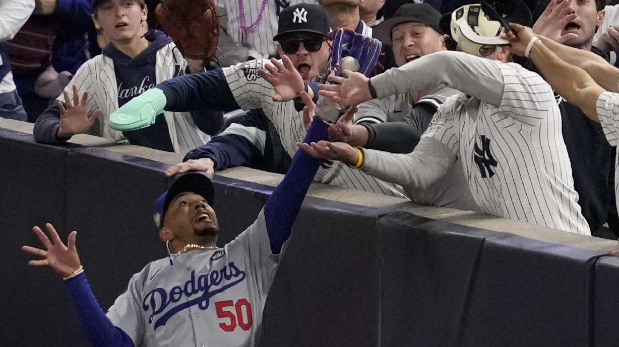 Fans interfere with a foul ball caught by Los Angeles Dodgers right fielder Mookie Betts during the first inning in Game 4 of the baseball World Series against the New York Yankees, on Oct. 29, 2024, in New York.