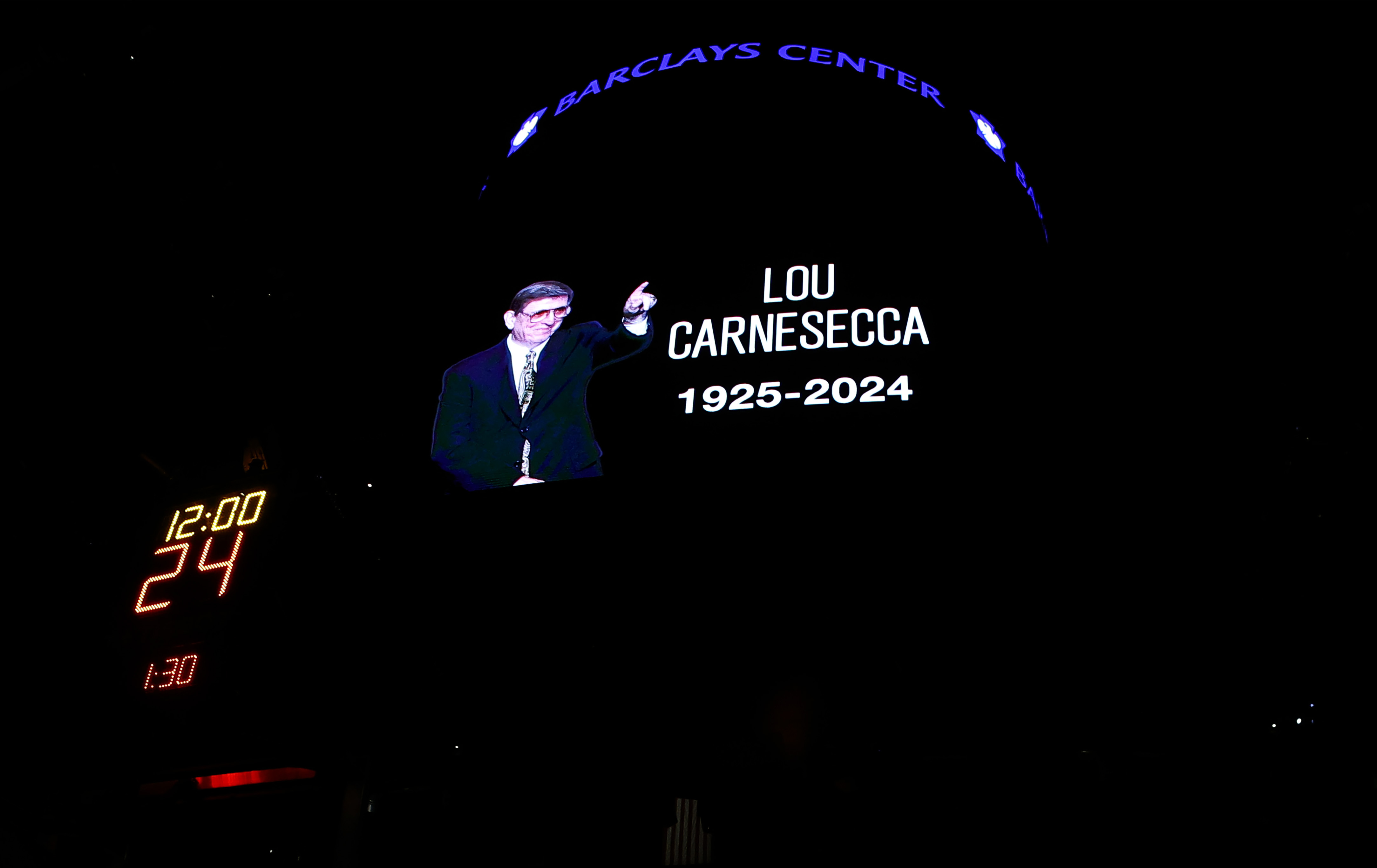 Fans pause for a moment of silence in memory of former St. John's men's basketball coach Lou Carnesecca before an NBA basketball game between the Orlando Magic and the Brooklyn Nets, Sunday, Dec. 1, 2024, in New York. 