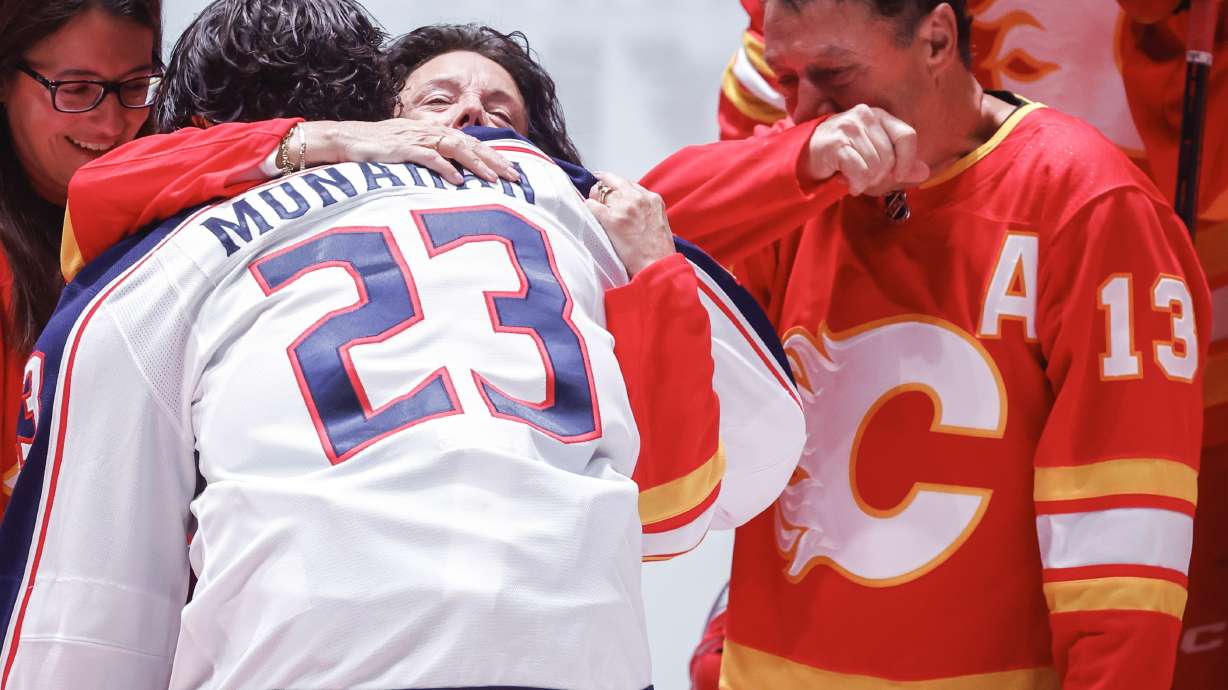 Columbus Blue Jackets' Sean Monahan hugs Johnny Gaudreau's mother Jane as his father Guy, right, looks on at centre ice prior to first period NHL hockey action against the Calgary Flames in Calgary on Tuesday, Dec. 3, 2024.THE CANADIAN PRESS/Jeff McIntosh/The Canadian Press via AP)