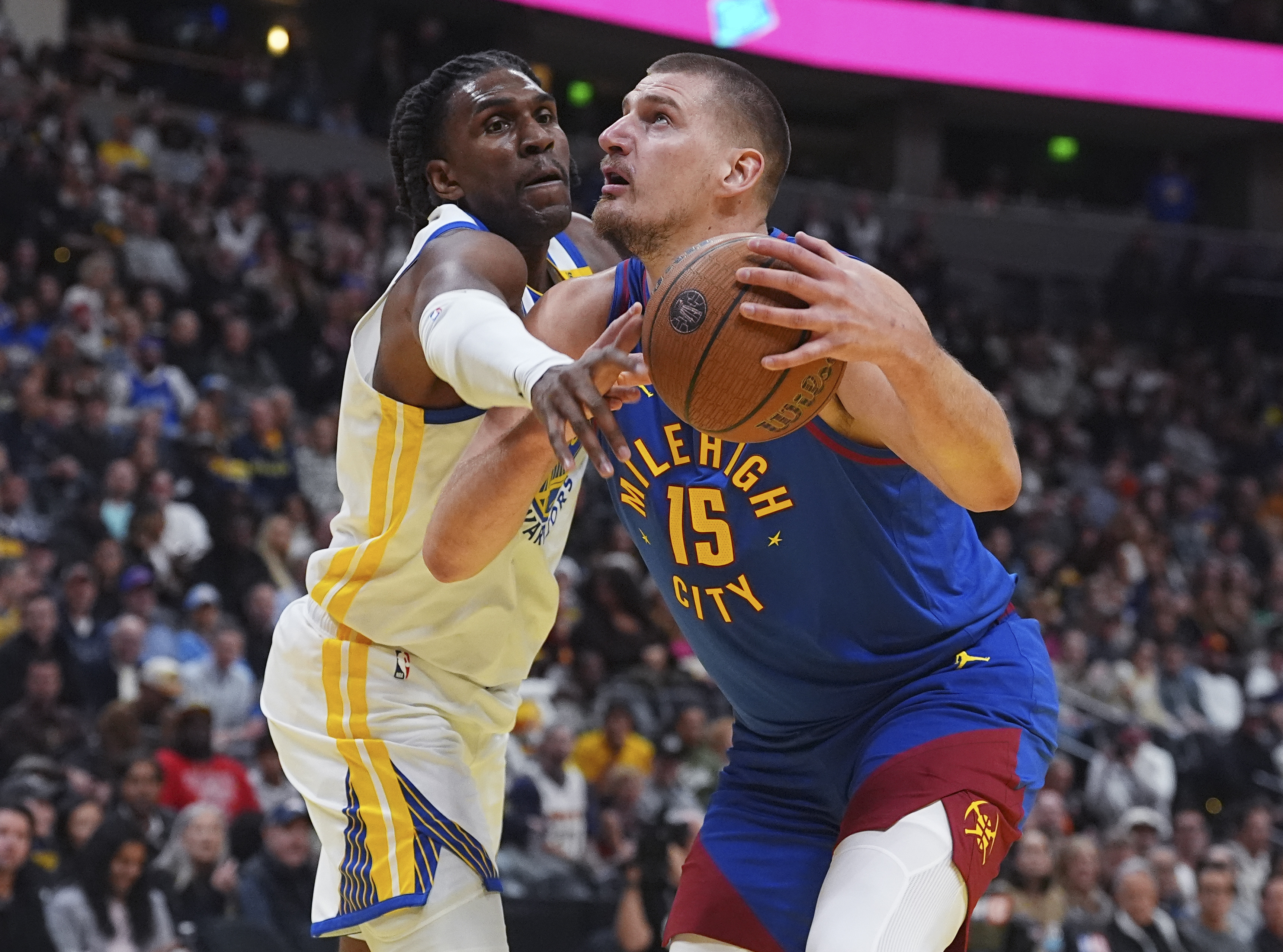Golden State Warriors forward Kevon Looney, left, knocks the ball out of the hands of Denver Nuggets center Nikola Jokic as he drives to the rim in the first half of an Emirates NBA Cup basketball game Tuesday, Dec. 3, 2024, in Denver.