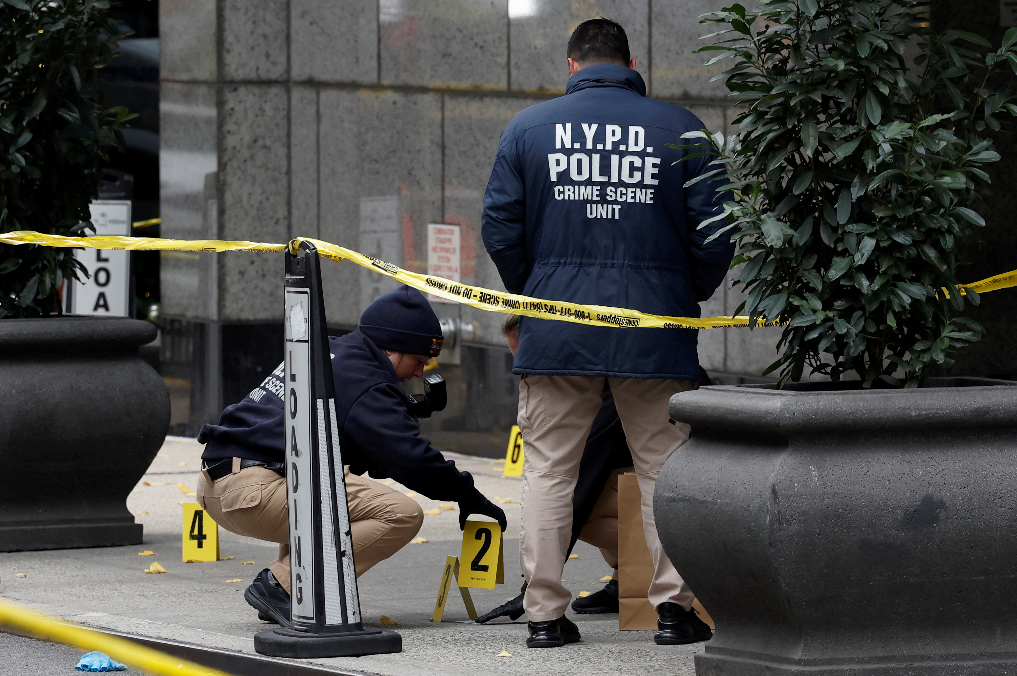 Members of the NYPD Crime Scene Unit work near evidence markers placed where shell casings were found at the scene where the CEO of UnitedHealthcare Brian Thompson was reportedly shot and killed in Midtown Manhattan, in New York City, Wednesday.