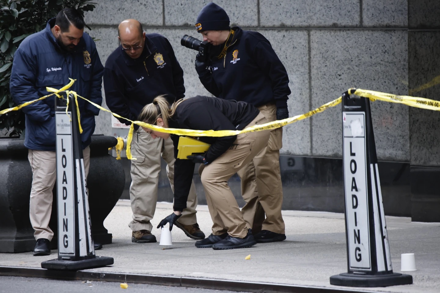 Members of the New York police crime scene unit pick up cups marking the spots where bullets lie as they investigate the scene outside the Hilton Hotel in midtown Manhattan where Brian Thompson, the CEO of UnitedHealthcare, was fatally shot Wednesday in New York.