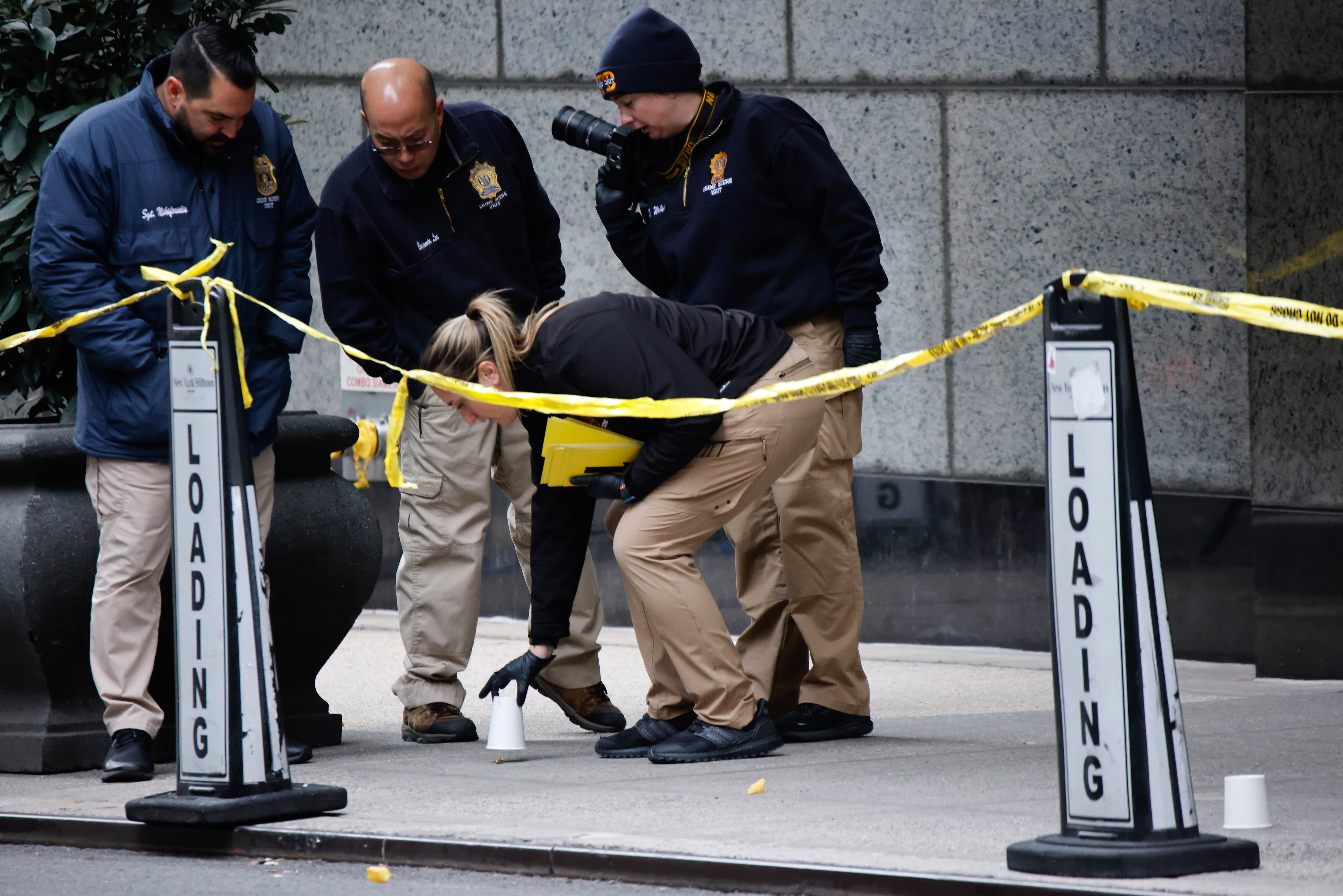 Members of the New York Police Department's Crime Scene Unit pick up cups marking the spots where bullets lie as they investigate the scene where Brian Thompson, the CEO of UnitedHealthcare, was fatally shot Wednesday in N.Y.