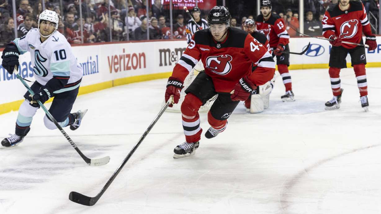 New Jersey Devils defenseman Luke Hughes (43) and Seattle Kraken center Matty Beniers (10) chase the puck during the third period of an NHL hockey game against the Seattle Kraken, Friday, Dec. 6, 2024, in Newark, N.J. Devils won 3-2.