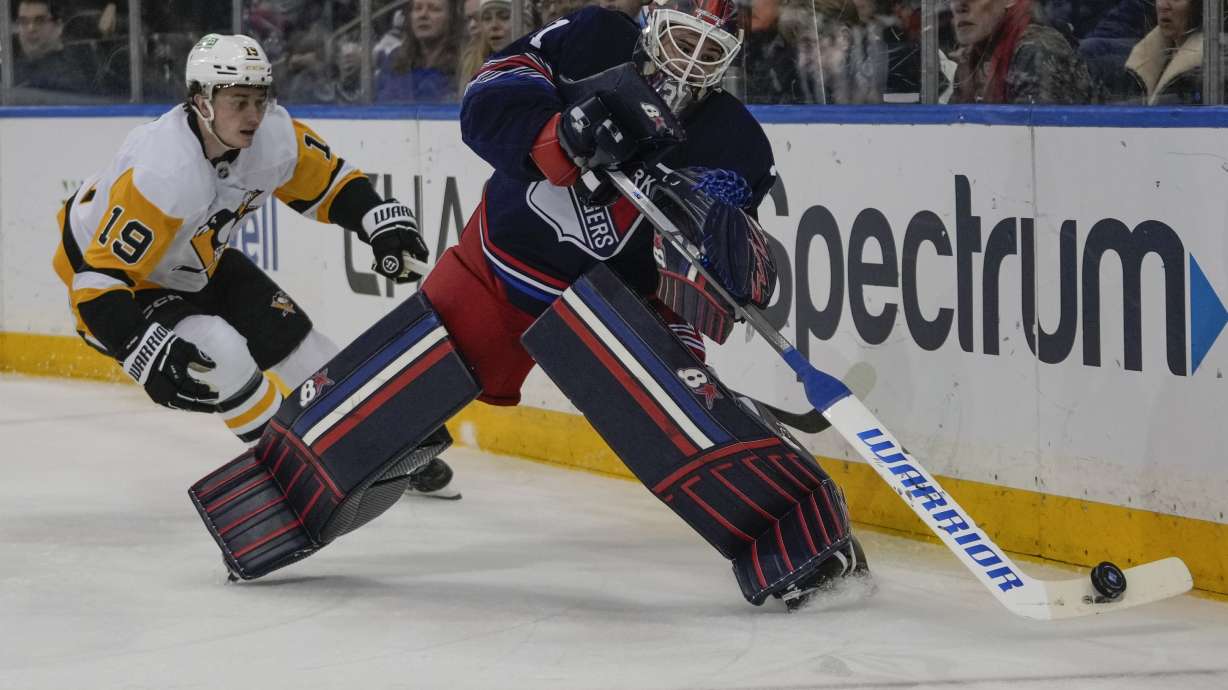 New York Rangers goaltender Igor Shesterkin passes to a teammate as Pittsburgh Penguins' Cody Glass (19) closes in during the first period of an NHL hockey game Friday, Dec. 6, 2024, in New York.