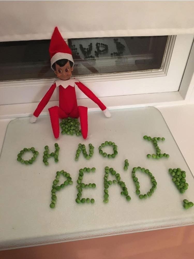 An Elf on the Shelf poses with peas on a table.