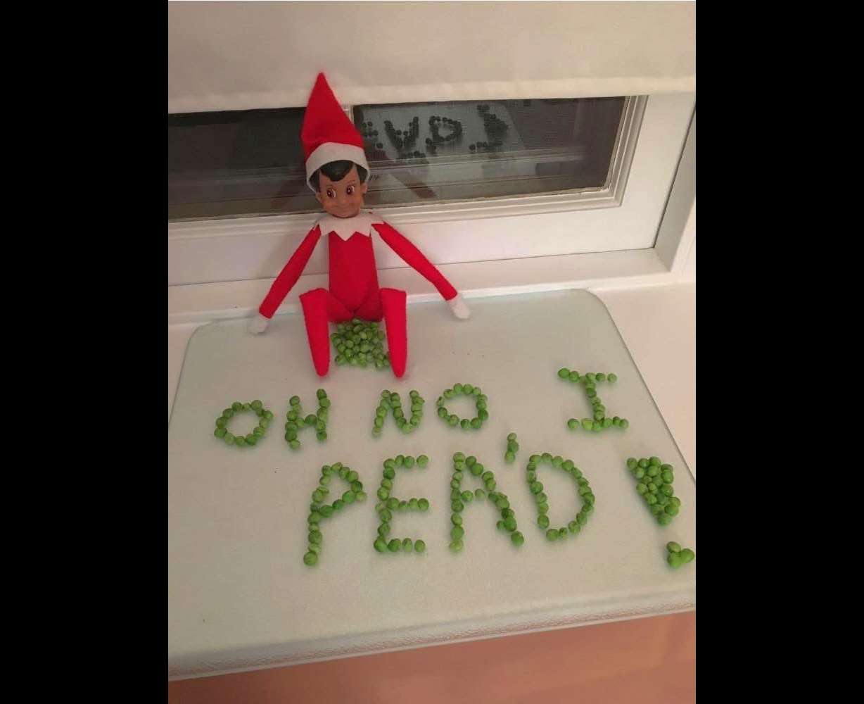 An Elf on the Shelf poses with peas on a table.