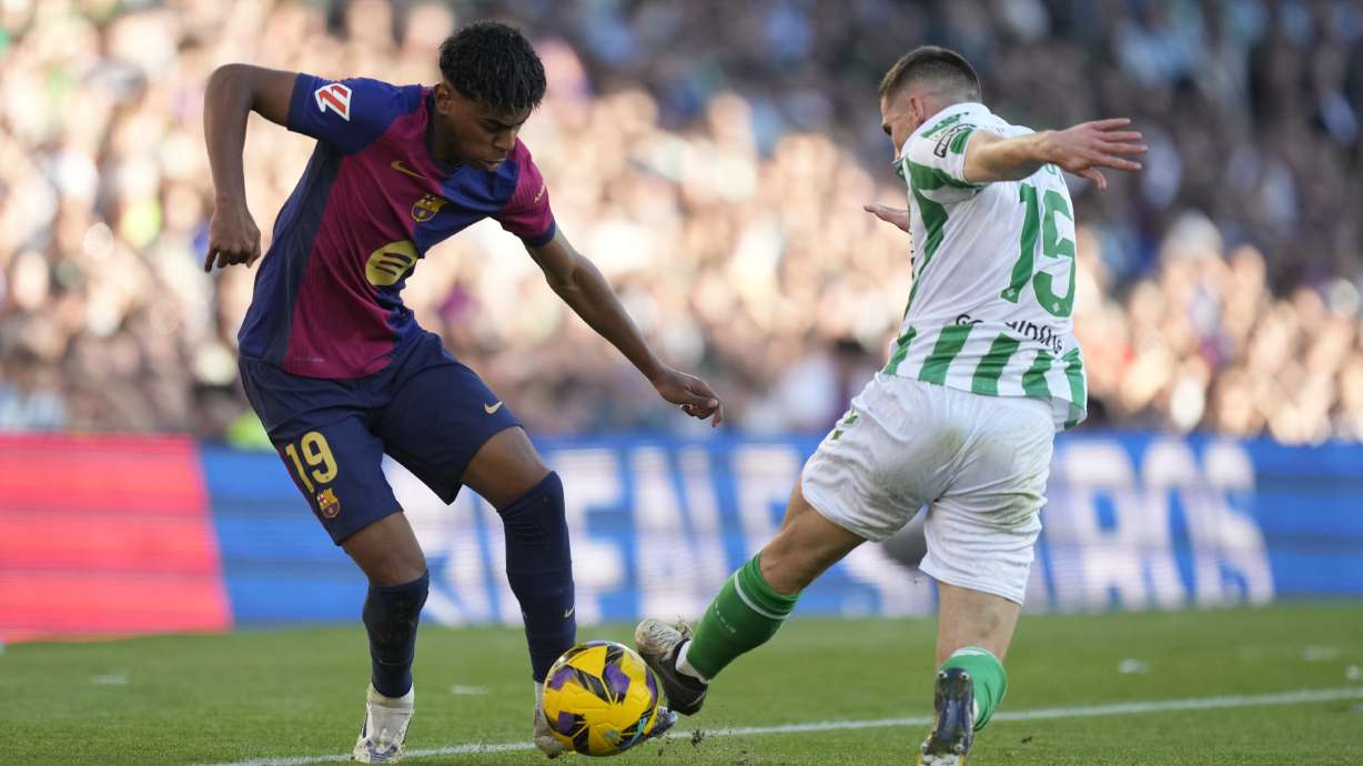 Barcelona's Lamine Yamal, left, challenges for the ball with Betis' Romain Perraud during a Spanish La Liga soccer match between Betis and Barcelona at the Benito Villamarin stadium in Seville, Spain, Saturday, Dec. 7, 2024.