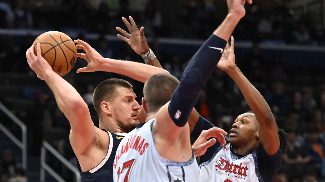 Denver Nuggets center Nikola Jokic, left, is defended by Washington Wizards center Jonas Valanciunas, center, and guard Carlton Carrington (8) during the second half of an NBA basketball game Saturday, Dec. 7, 2024, in Washington.
