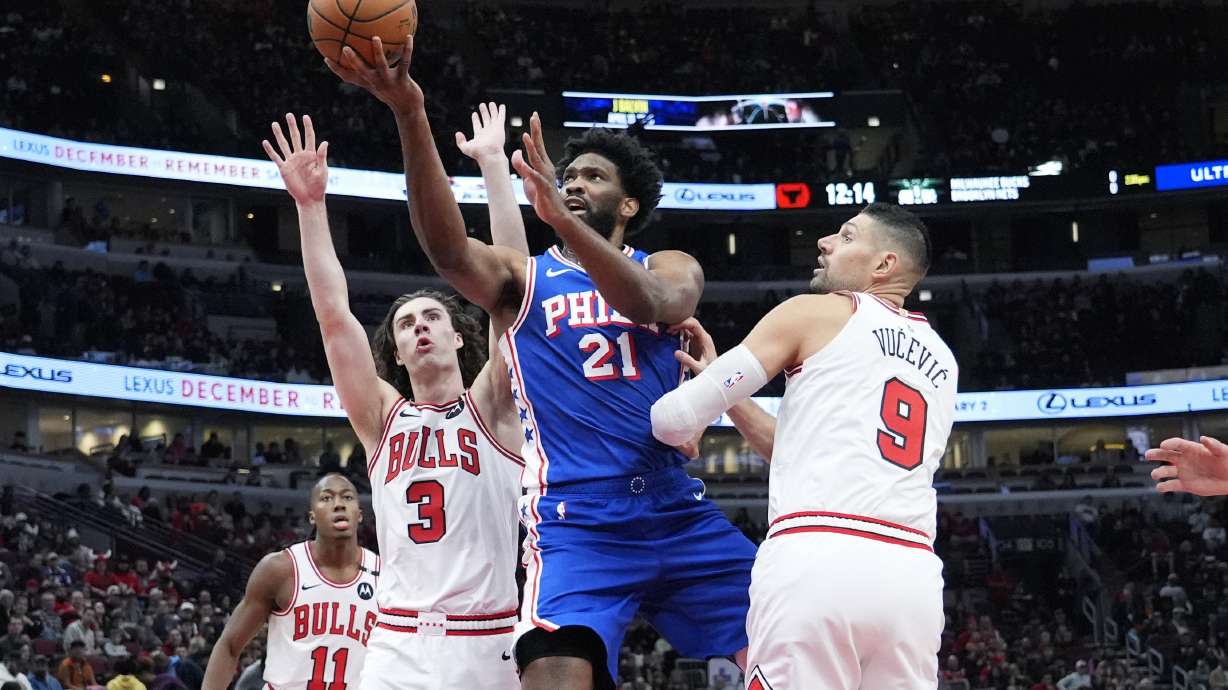 Philadelphia 76ers center Joel Embiid (21) drives to the basket against Chicago Bulls guard Josh Giddey (3) and center Nikola Vucevic (9) during the first half of an NBA basketball game in Chicago, Sunday, Dec. 8, 2024.