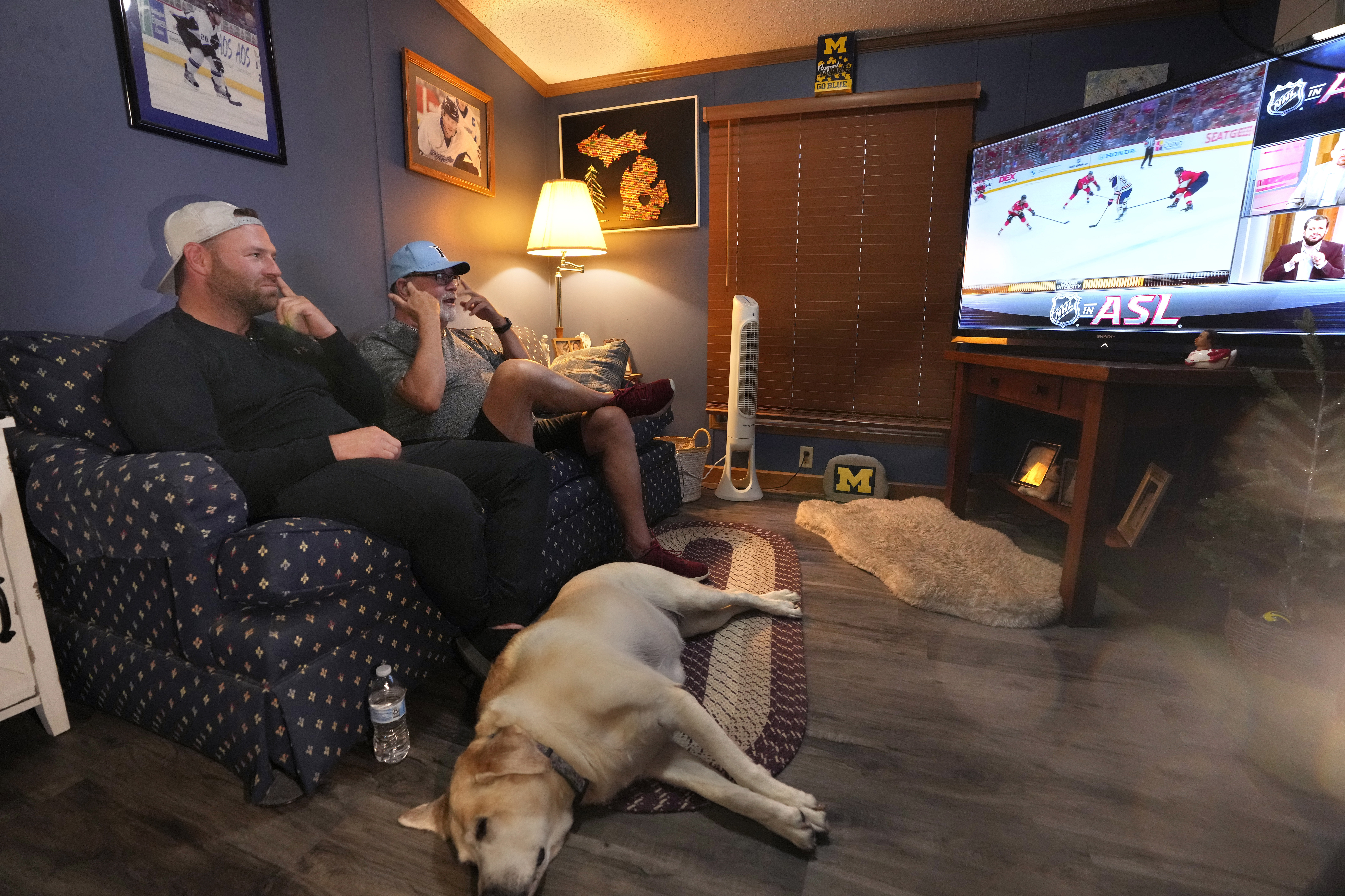 FILE - Bob Madden, center, and his son Jonathan, left, watch the Stanley Cup hockey final from a couch, Monday, June 10, 2024 in Genoa Township, Mich.