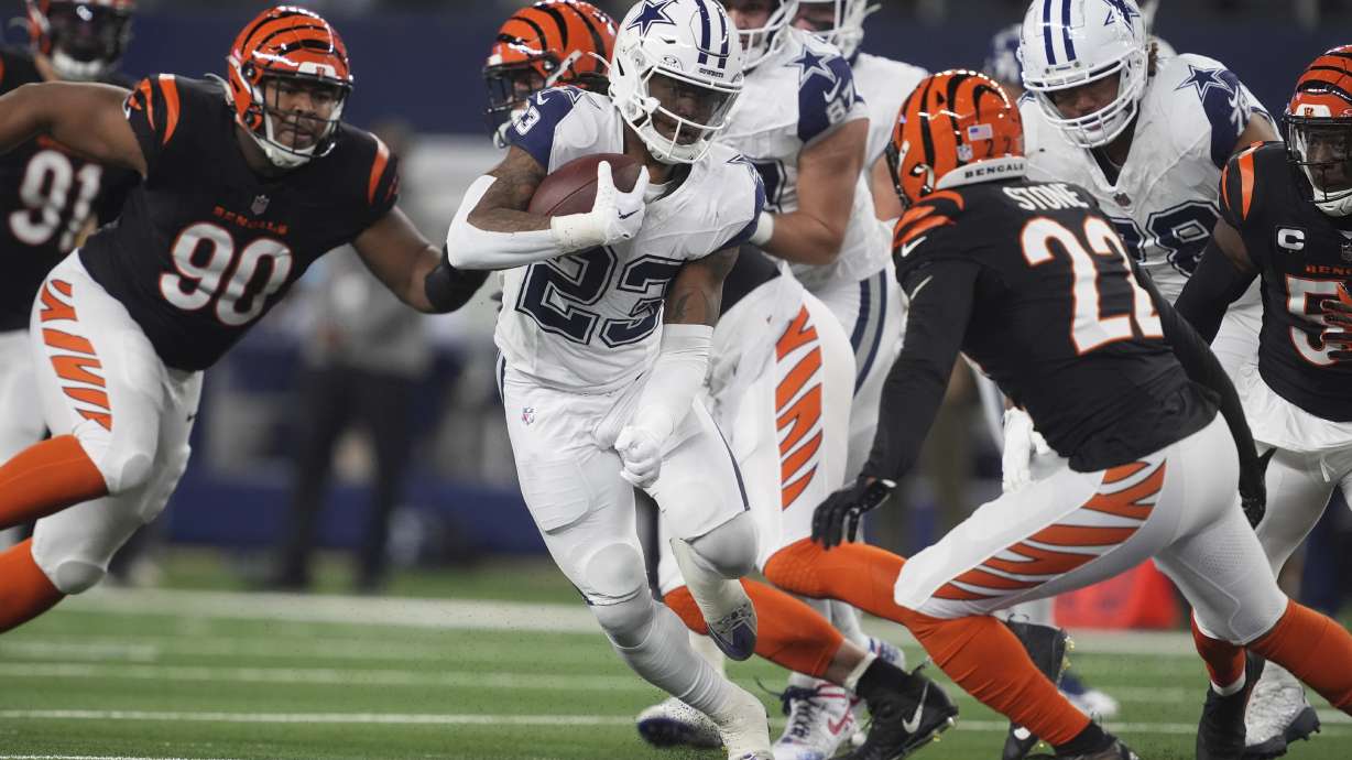 Dallas Cowboys running back Rico Dowdle (23) runs with the ball as Cincinnati Bengals defensive tackle Kris Jenkins Jr. (90) and Cincinnati Bengals safety Geno Stone (22) move in during the first half of an NFL football game, Monday, Dec. 9, 2024, in Arlington, Texas.