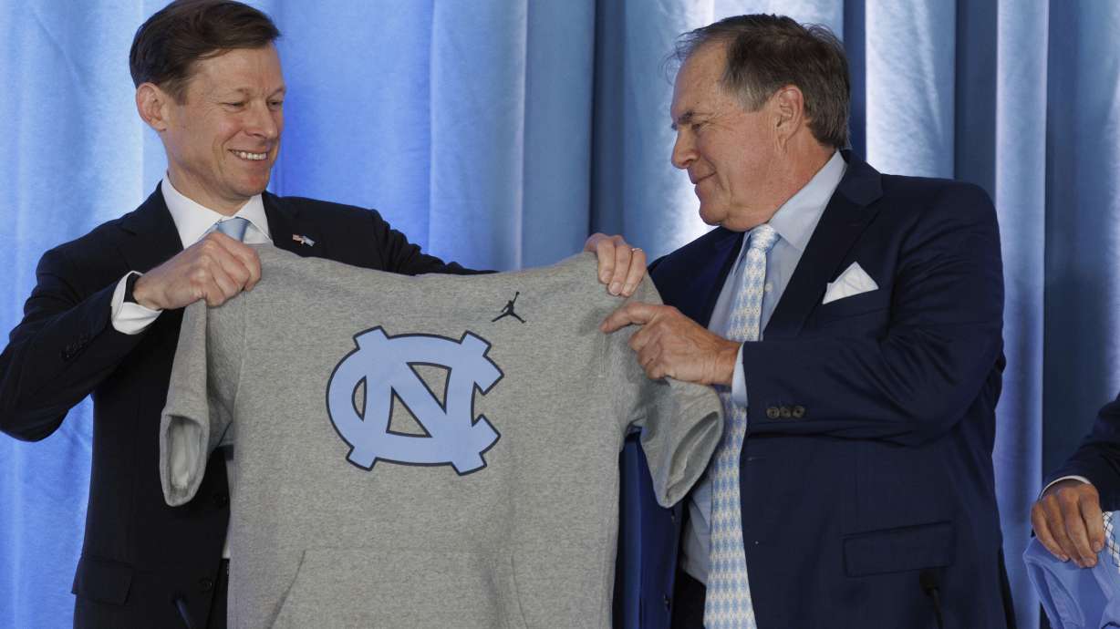 University of North Carolina Chancellor Lee Roberts, left, hands. new North Carolina coach Bill Belichick, right, a sleeveless UNC hoodie during an NCAA college football press conference in Chapel Hill, N.C., Thursday, Dec. 12, 2024.