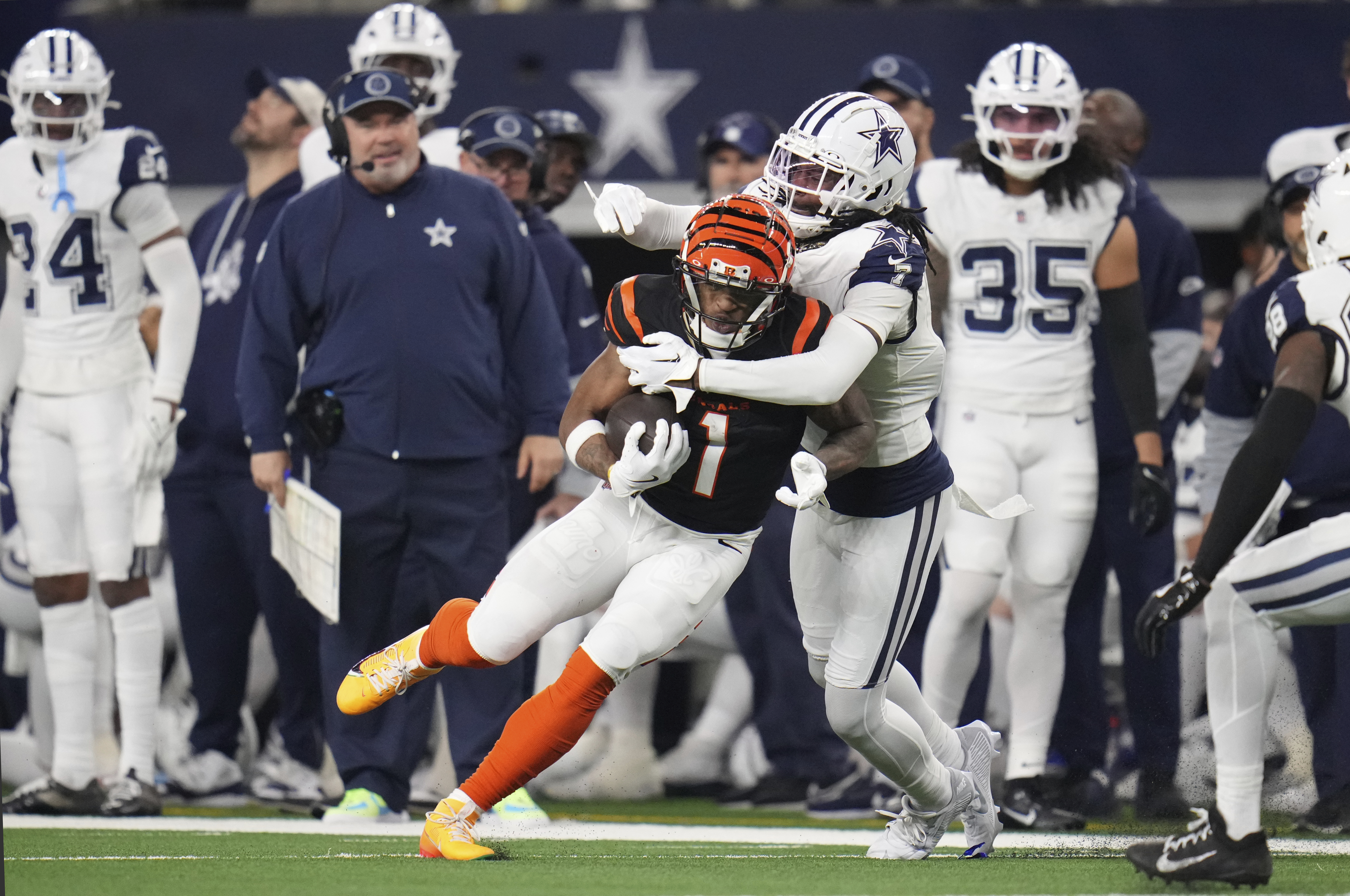 Cincinnati Bengals wide receiver Ja'Marr Chase (1) is tackled by Dallas Cowboys cornerback Trevon Diggs (7) as Dallas Cowboys head coach Mike McCarthy looks on at left during the first half of an NFL football game, Monday, Dec. 9, 2024, in Arlington, Texas.