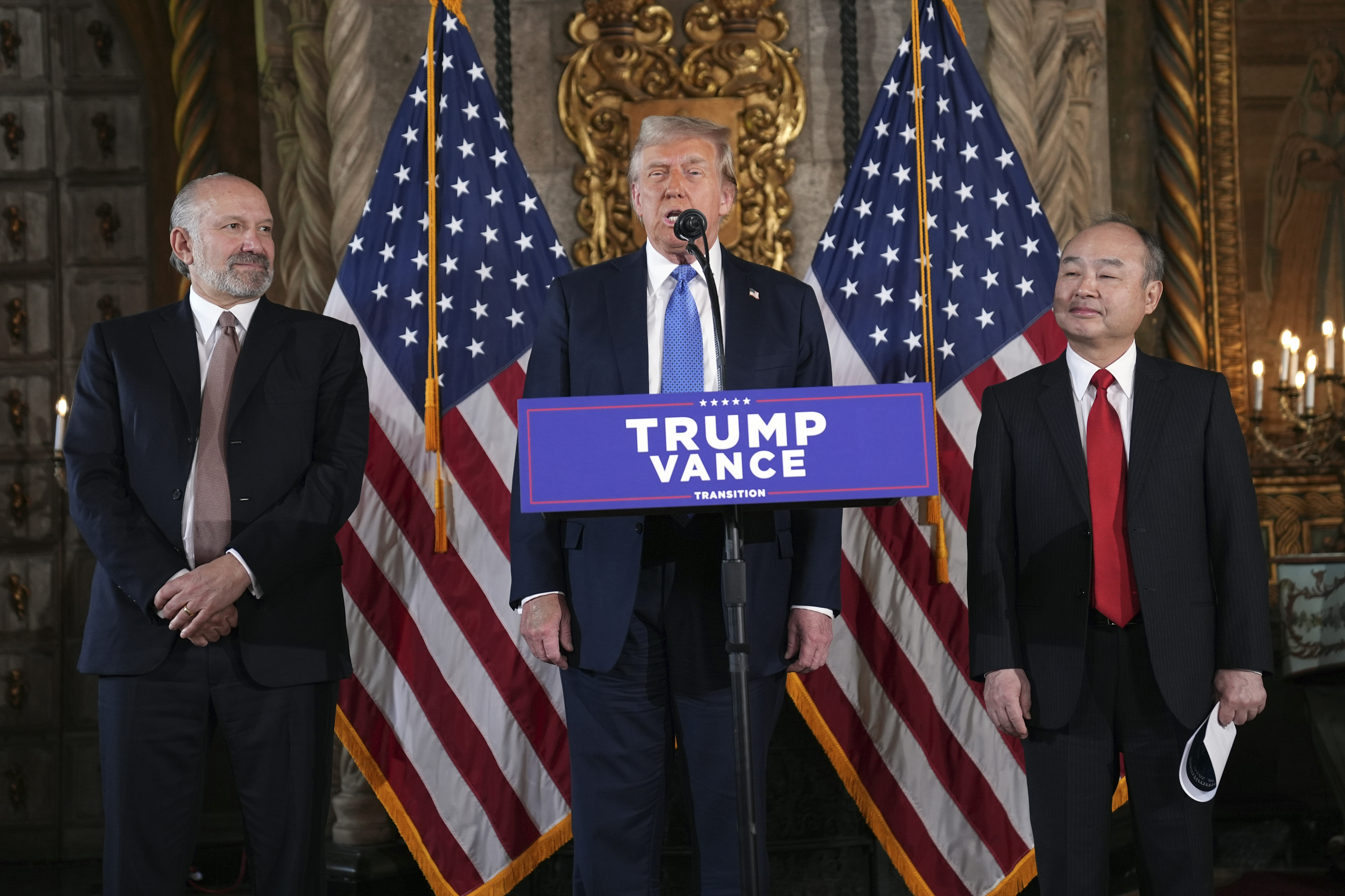 President-elect Donald Trump speaks during a news conference at Mar-a-Lago, Monday, in Palm Beach, Fla., as SoftBank Group CEO Masayoshi Son, right, and Commerce Secretary nominee Howard Lutnick listen. Trump announced that SoftBank would invest $100 billion in the U.S. over the next four years.