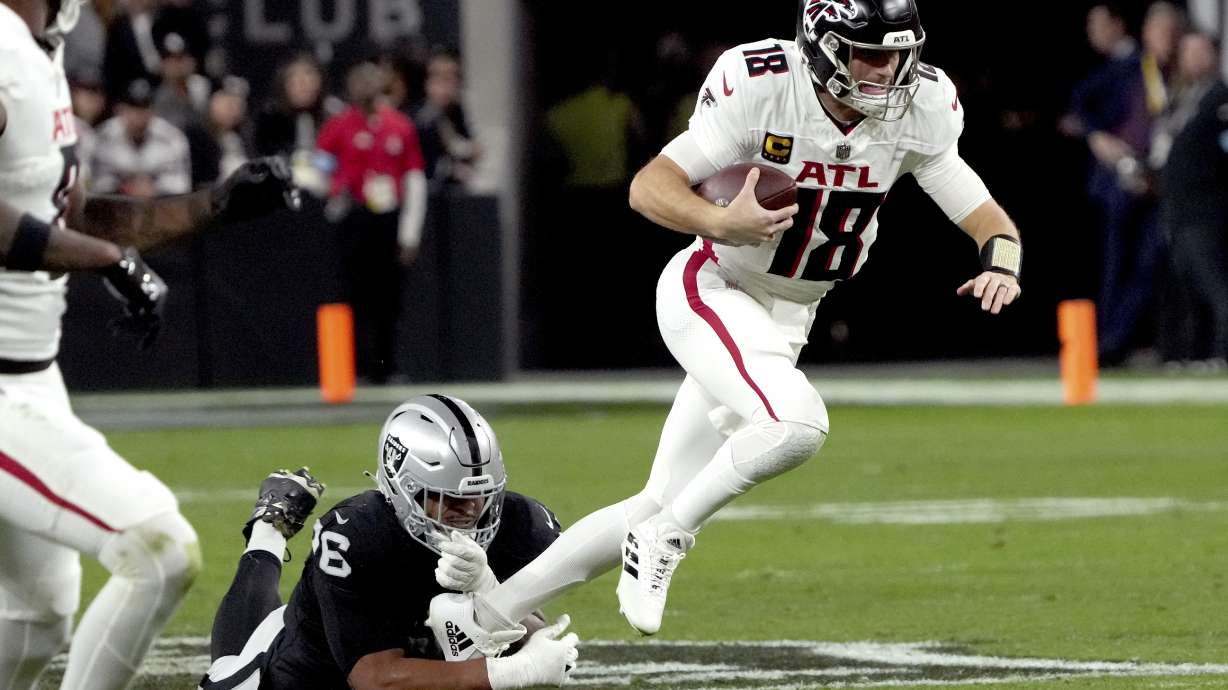 Atlanta Falcons quarterback Kirk Cousins (18) is tripped up by Las Vegas Raiders defensive tackle Jonah Laulu (96) during the first half of an NFL football game, Monday, Dec. 16, 2024, in Las Vegas.