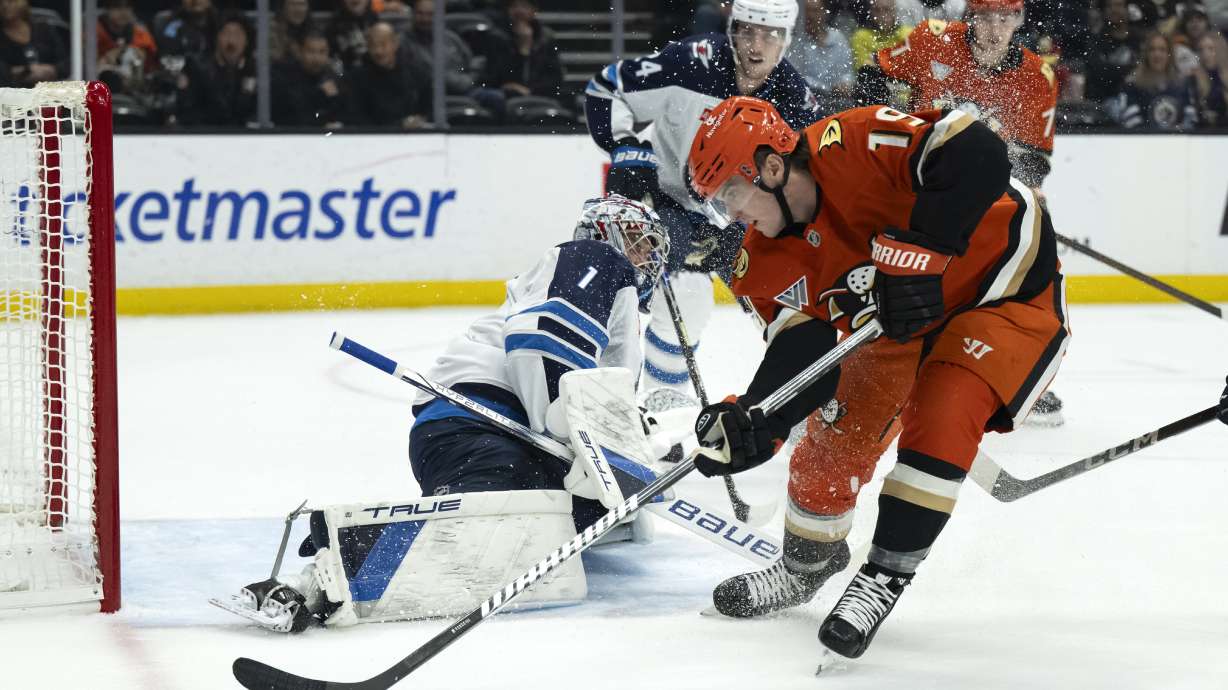 Anaheim Ducks right wing Troy Terry (19) controls the puck in front of Winnipeg Jets goaltender Eric Comrie (1) during the first period of an NHL hockey game, Wednesday, Dec. 18, 2024, in Anaheim, Calif.