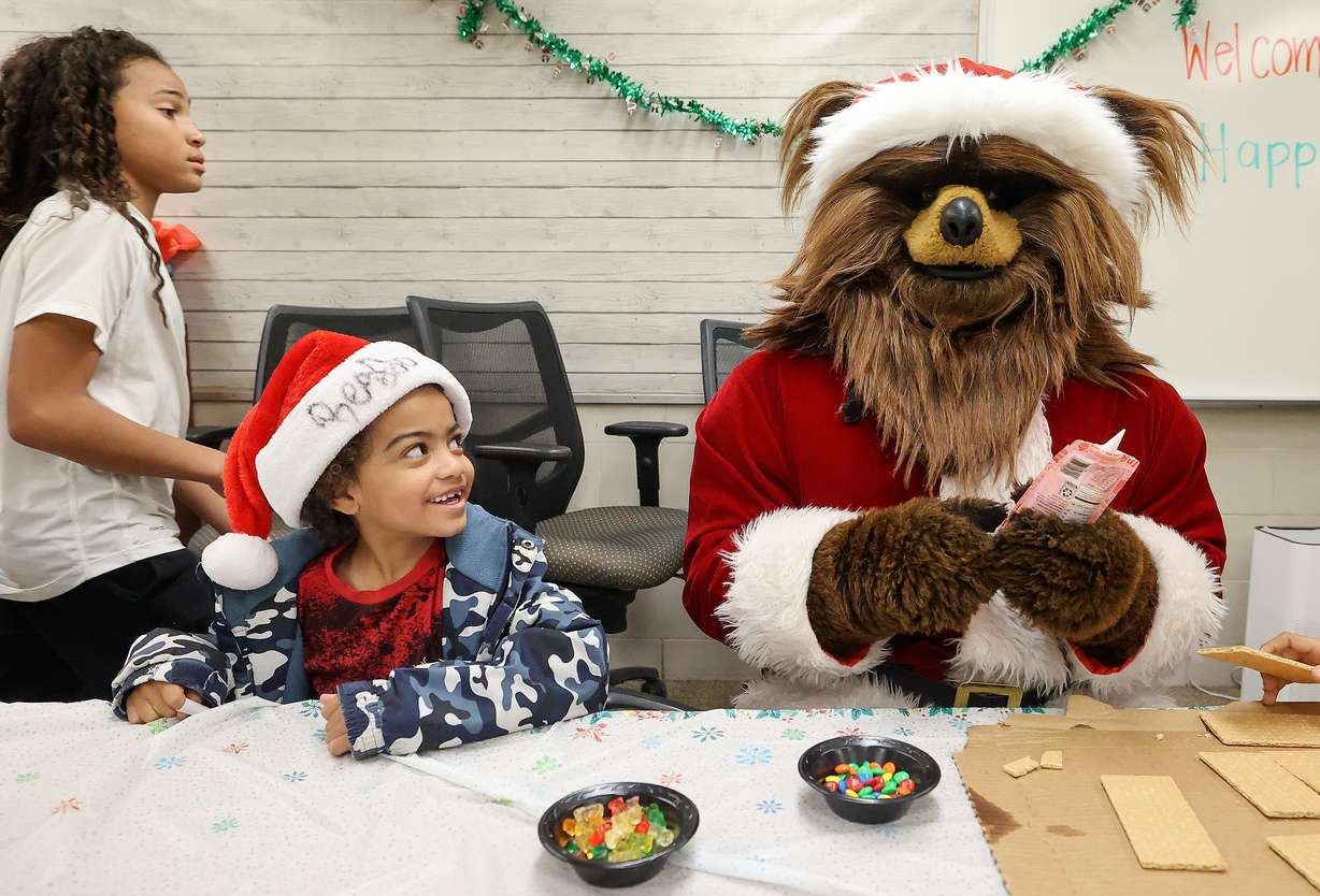Lyrik Edgar helps Jazz Bear build a gingerbread house during a Christmas party with Utah Jazz forward Taylor Hendricks and students at Arcadia Elementary School in Taylorsville on Wednesday, Dec. 18, 2024. Attending students received a Jazz swag bag and Walmart gift card.