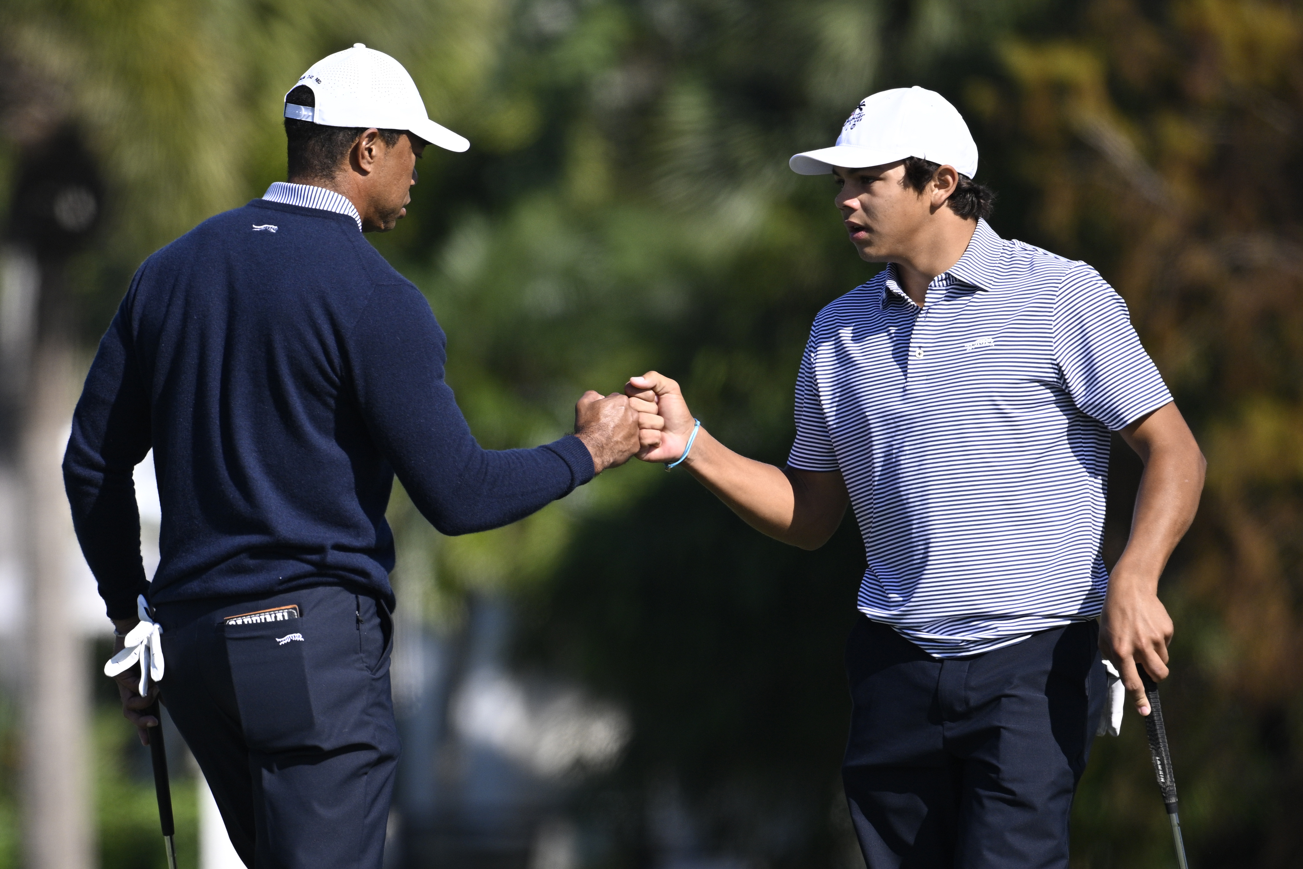 Charlie Woods, right, gets a fist bump from his father, Tiger Woods after making their putt on the fourth green during the first round of the PNC Championship golf tournament, Saturday, Dec. 21, 2024 in Orlando.