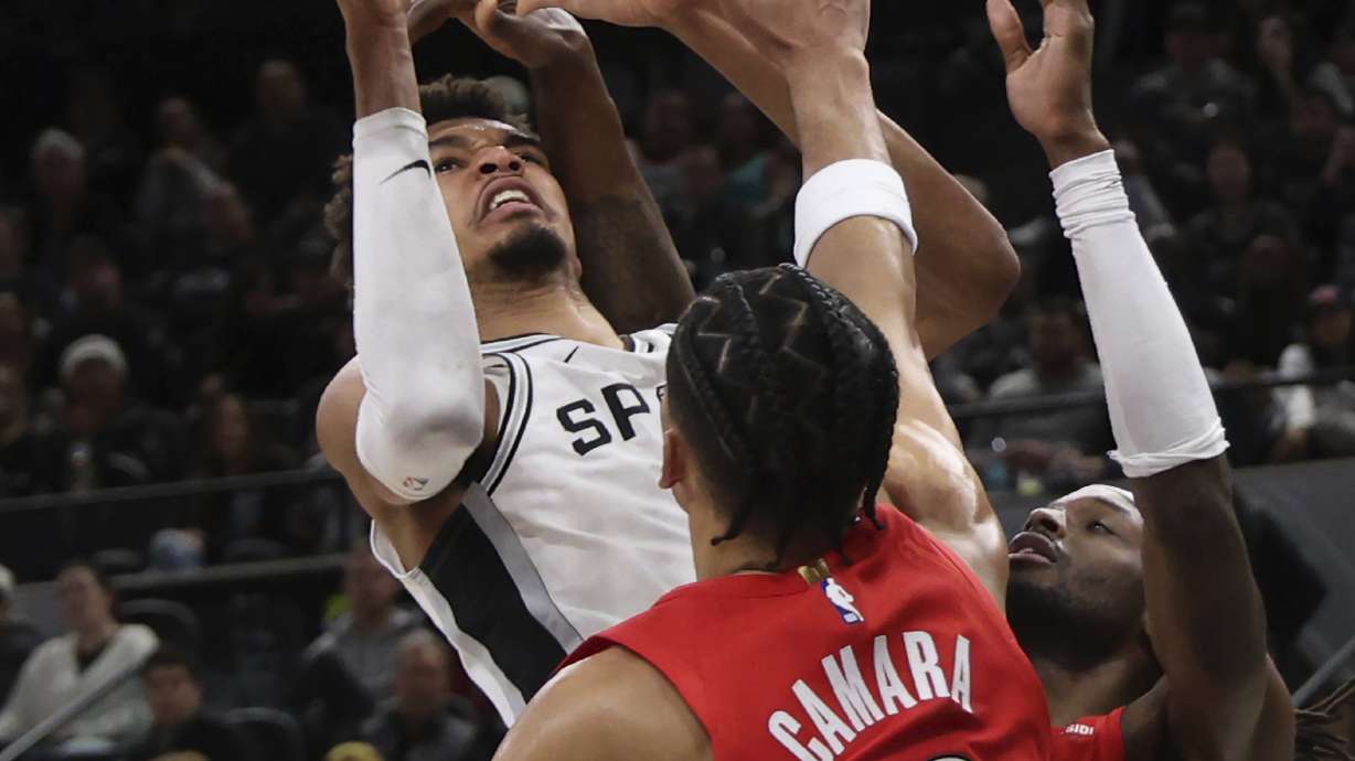 San Antonio Spurs center Victor Wembanyama, left, attempts a shot against Portland Trail Blazers forward Jerami Grant, right, and forward Toumani Camara (33) during the first half of an NBA basketball game in San Antonio, Saturday, Dec. 21, 2024.
