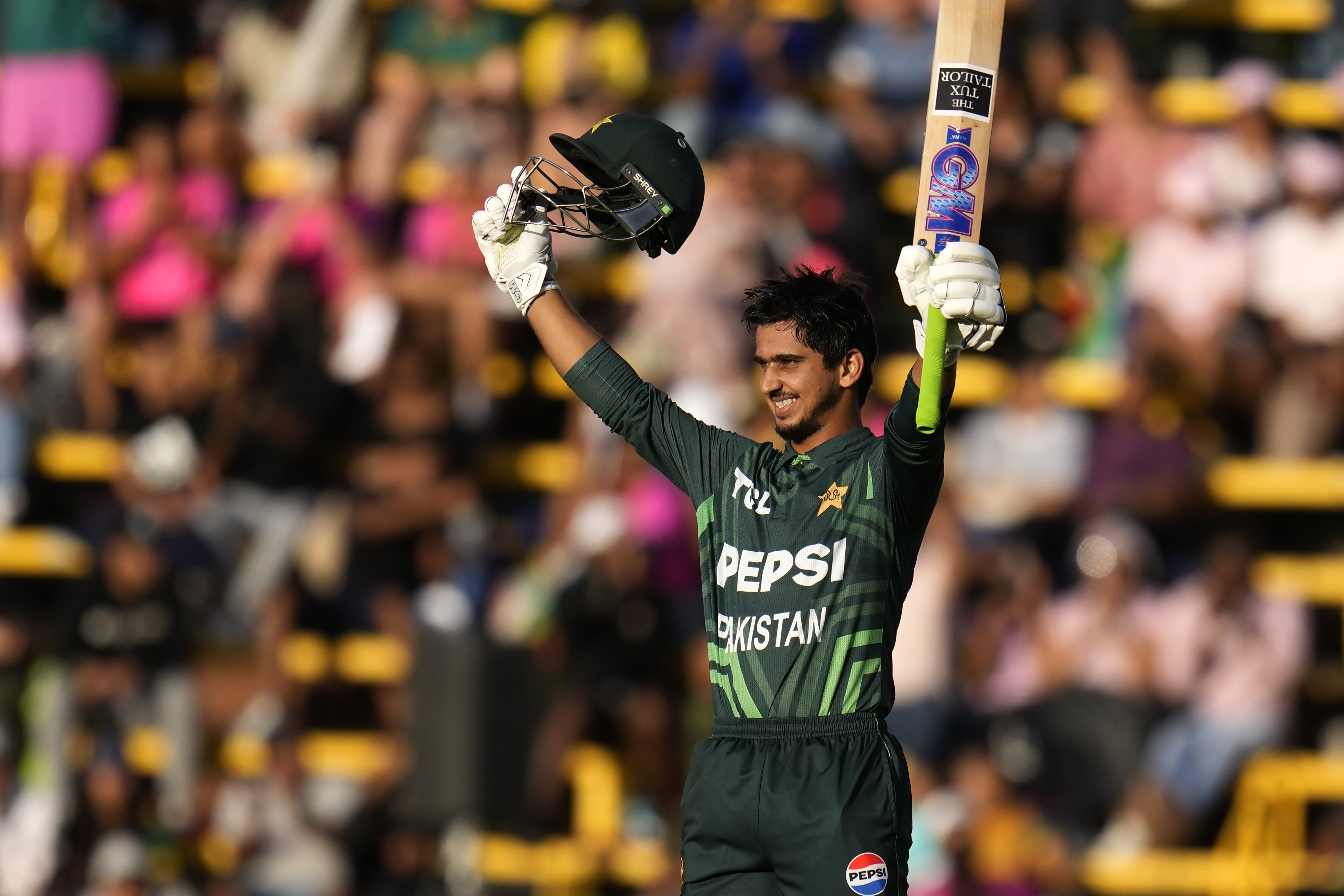 Pakistan's Saim Ayub raises his bat and hemet after reaching his century during the third International cricket match between South Africa and Pakistan, at the Wanderers stadium in Johannesburg, South Africa, Sunday, Dec. 22, 2024. 