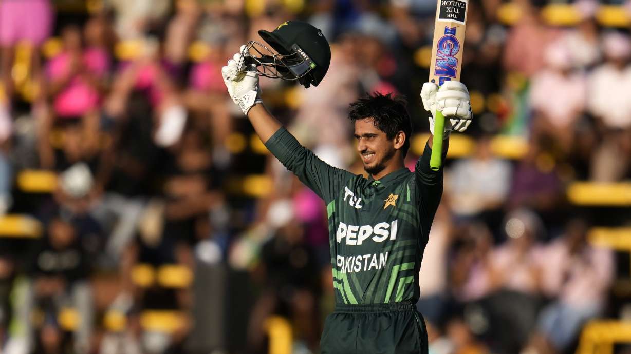 Pakistan's Saim Ayub raises his bat and hemet after reaching his century during the third International cricket match between South Africa and Pakistan, at the Wanderers stadium in Johannesburg, South Africa, Sunday, Dec. 22, 2024.