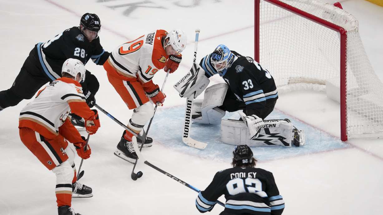 Anaheim Ducks right wing Troy Terry (19) shoots as defenseman Jackson LaCombe (2) assists while Utah Hockey Club goaltender Jaxson Stauber (33) defends with defenseman Ian Cole (28) and center Logan Cooley (92) during the second period of an NHL hockey game, Sunday, Dec. 22, 2024, in Salt Lake City.