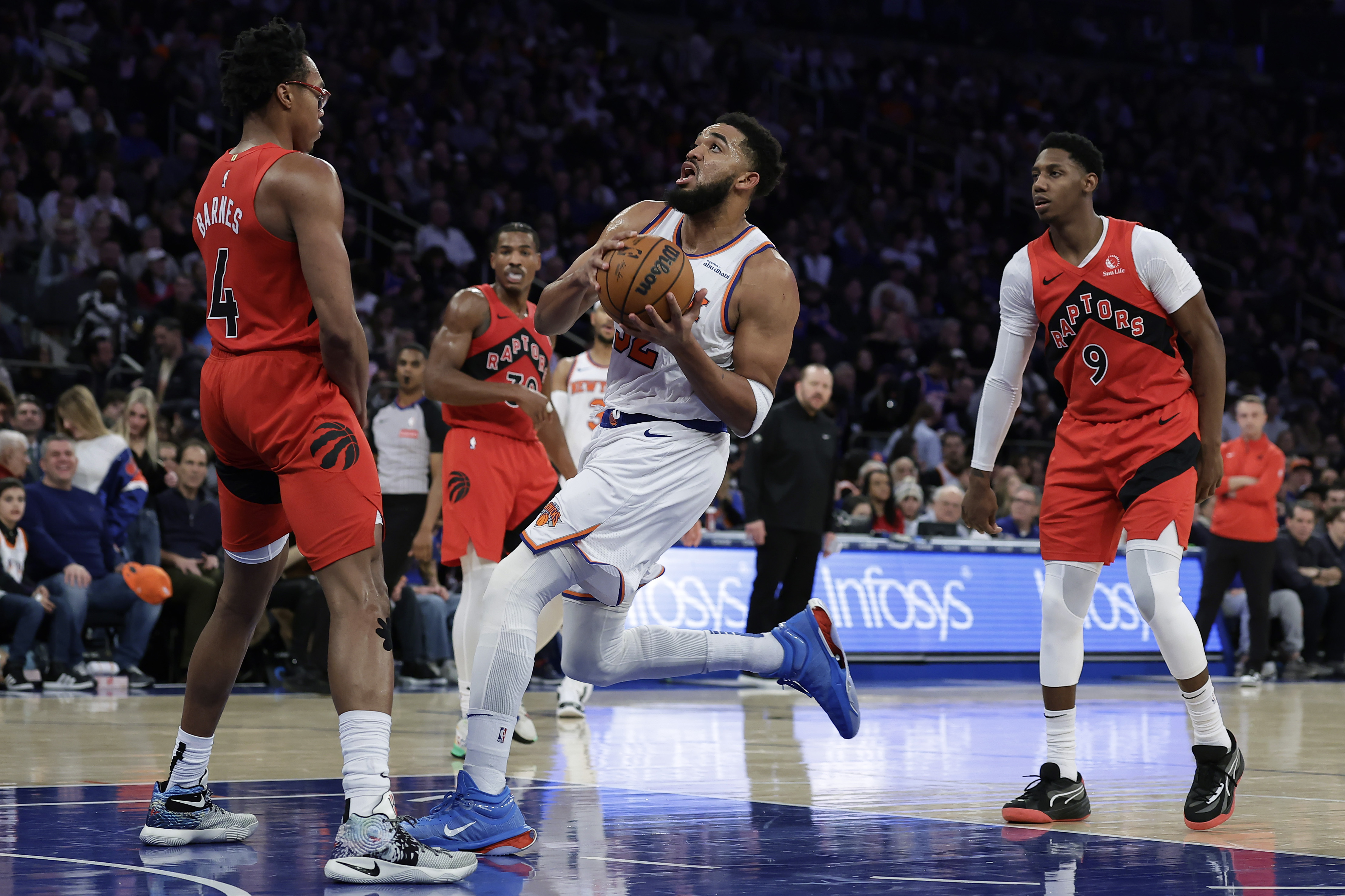 New York Knicks center Karl-Anthony Towns, center, drives to the basket between Toronto Raptors forward Scottie Barnes (4) and RJ Barrett (9) during the second half of an NBA basketball game Monday, Dec. 23, 2024, in New York.