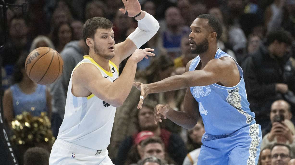 Cleveland Cavaliers' Evan Mobley, right, passes around Utah Jazz' Walker Kessler during the first half of an NBA basketball game in Cleveland, Monday, Dec. 23, 2024.
