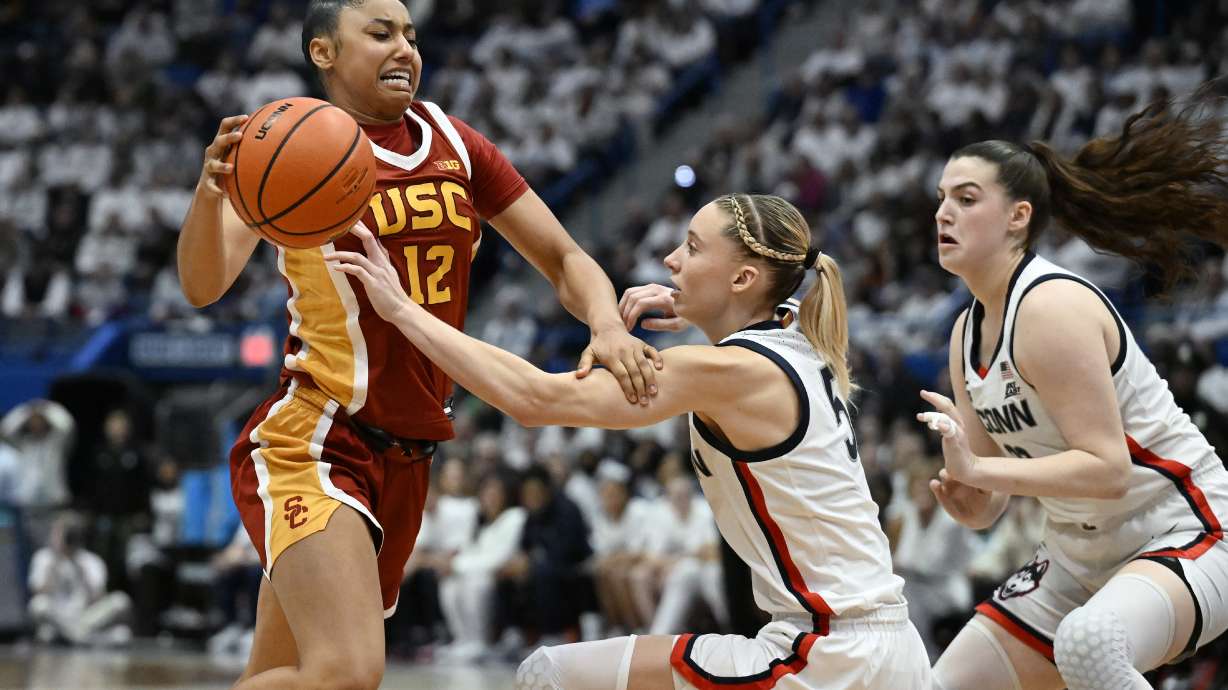 Southern California guard JuJu Watkins, left, drives to the basket as UConn guards Paige Bueckers, center, and Morgan Cheli, right, defend in the second half of an NCAA college basketball game, Saturday, Dec. 21, 2024, in Hartford, Conn.