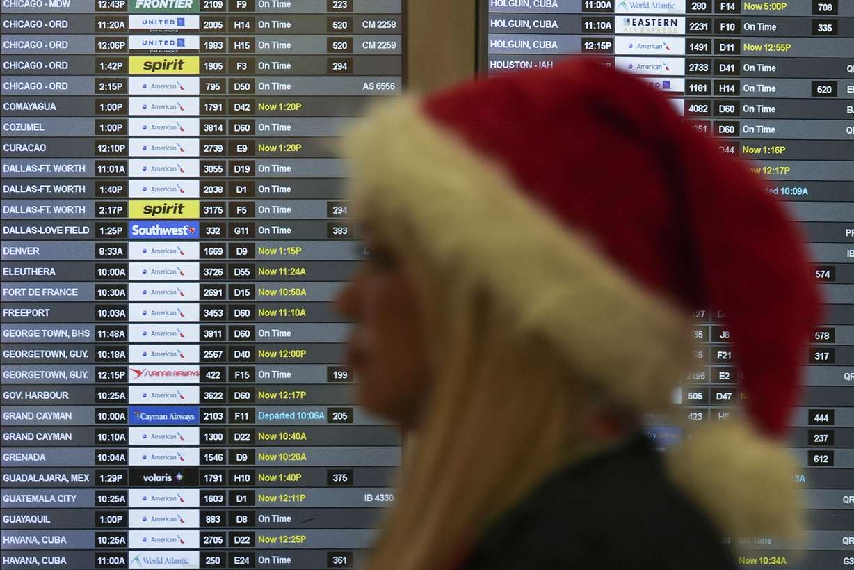 An employee wearing a Santa Claus hat walks past boards showing flight delays, in the American Airlines terminal at Miami International Airport, on Christmas Eve, Tuesday, in Miami.