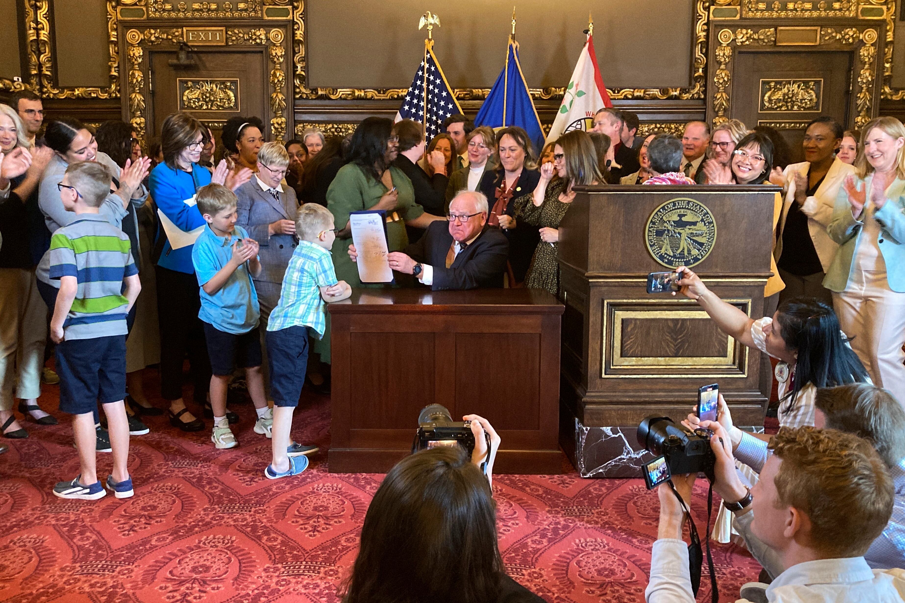 Democratic Minnesota Gov. Tim Walz jokes with kids as he shows off a bill he signed at the State Capitol in St. Paul, Minn., on May 25, 2023, to establish a paid family and medical leave program in the state starting in 2026.