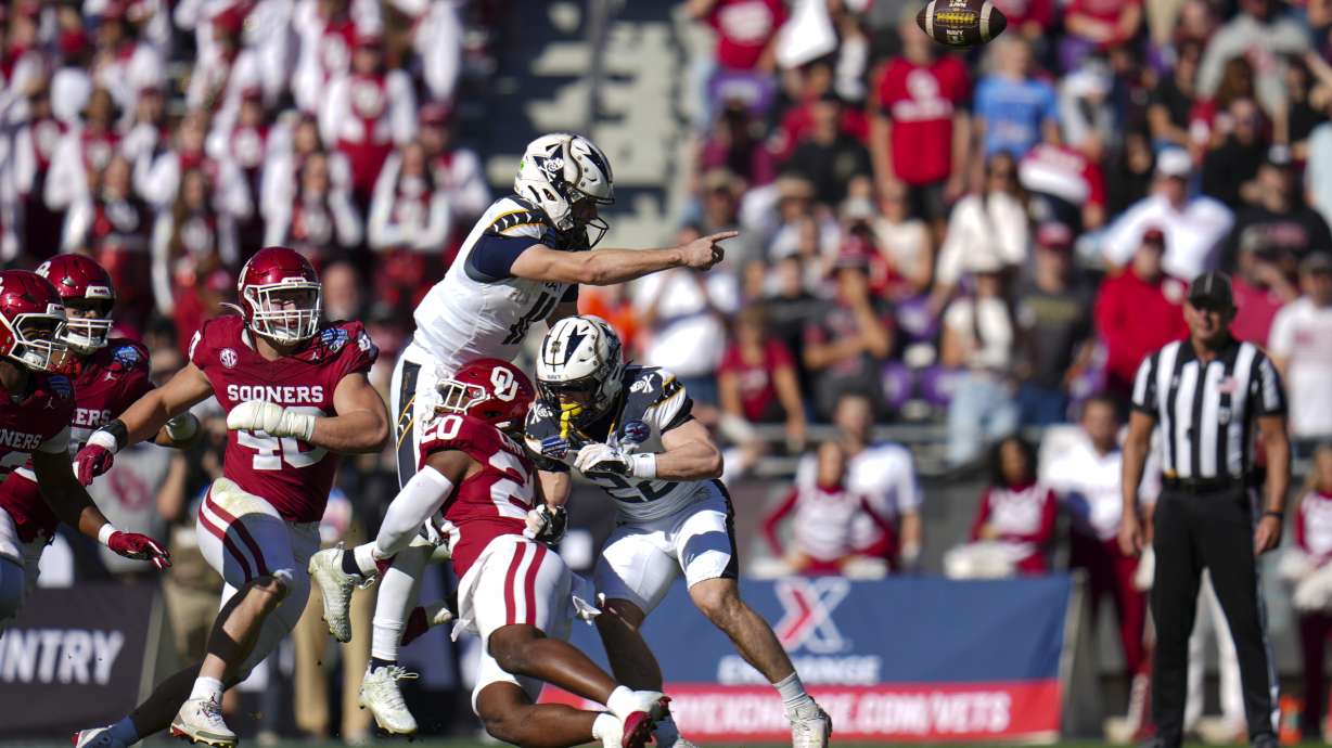 Navy quarterback Blake Horvath, top left, takes a hit from Oklahoma linebacker Lewis Carter (20) while attempting a pass during the first half of the Armed Forces Bowl NCAA college football game, Friday, Dec. 27, 2024, in Fort Worth, Texas.