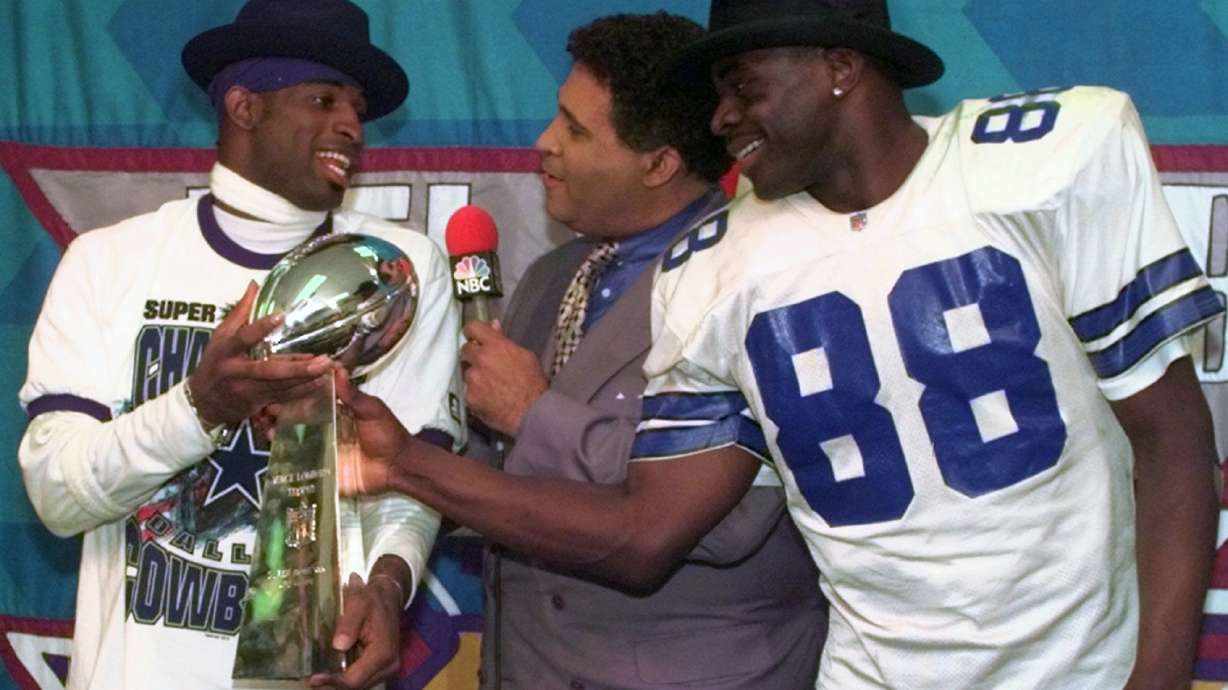 Dallas Cowboys cornerback Deion Sanders, left, and running back Michael Irvin (88) share the Vince Lombardi trophy as NBC commentator Greg Gumbel interviews the two after Super Bowl XXX in Tempe, Ariz., Sunday, Jan. 28, 1996.