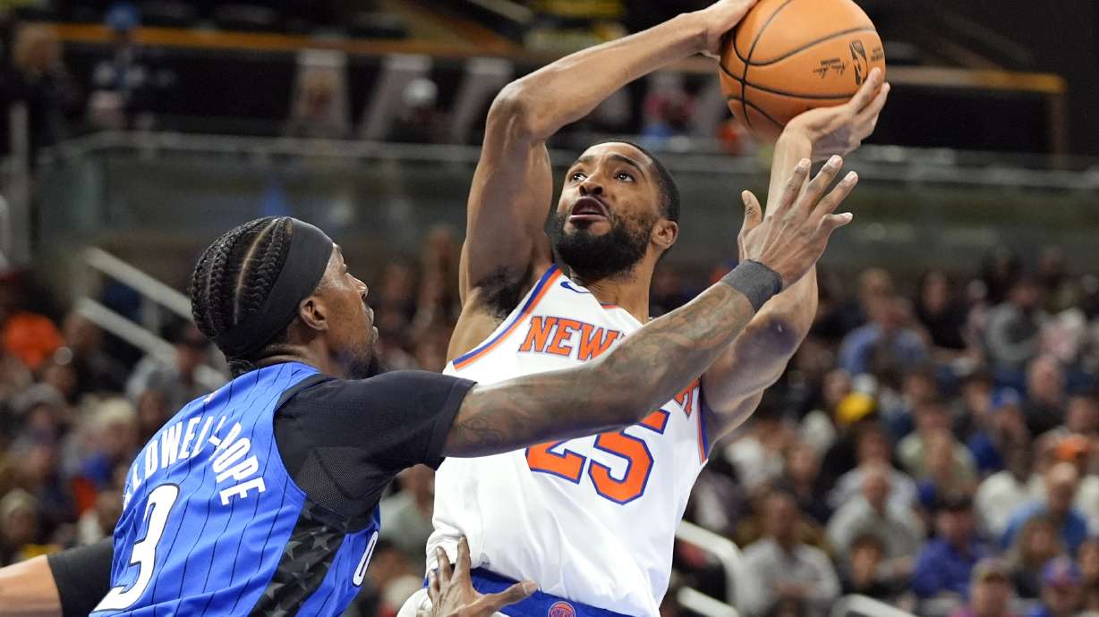 New York Knicks forward Mikal Bridges, right, takes a shot over Orlando Magic guard Kentavious Caldwell-Pope (3) during the first half of an NBA basketball game, Friday, Dec. 27, 2024, in Orlando, Fla.