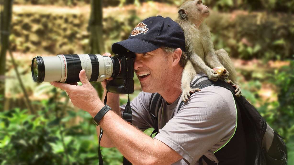 Jeffrey Allred shoots photos as a long-tailed macaque monkey sits on his shoulder in the Sacred Monkey Forest Sanctuary in Ubud, Indonesia, on Nov. 22, 2019. Allred is retiring after a lifetime in photography.