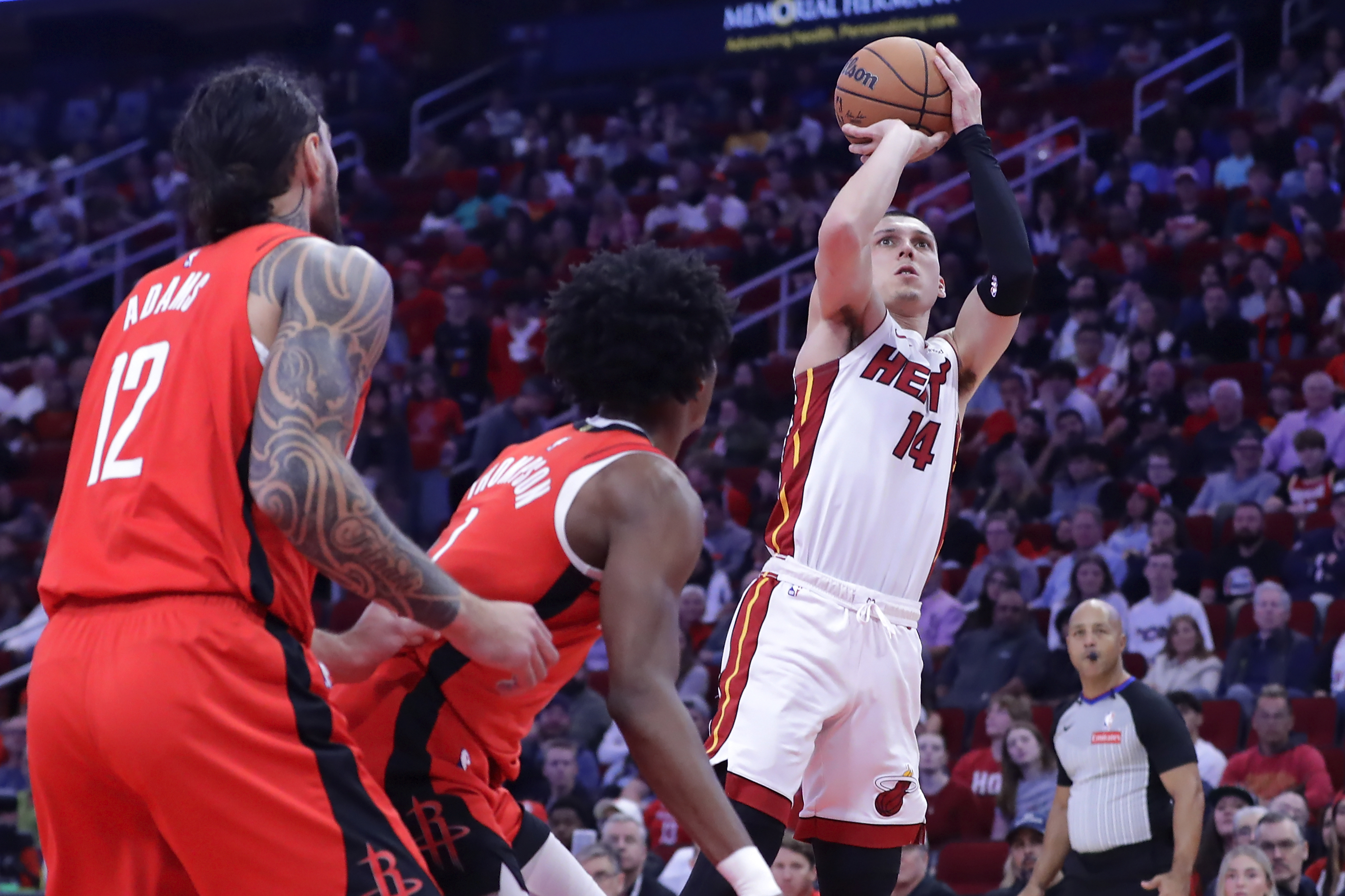 Miami Heat guard Tyler Herro (14) shoots a three-point shot as Houston Rockets center Steven Adams (12) and forward Amen Thompson, center, look on during the first half of an NBA basketball game Sunday, Dec. 29, 2024, in Houston.