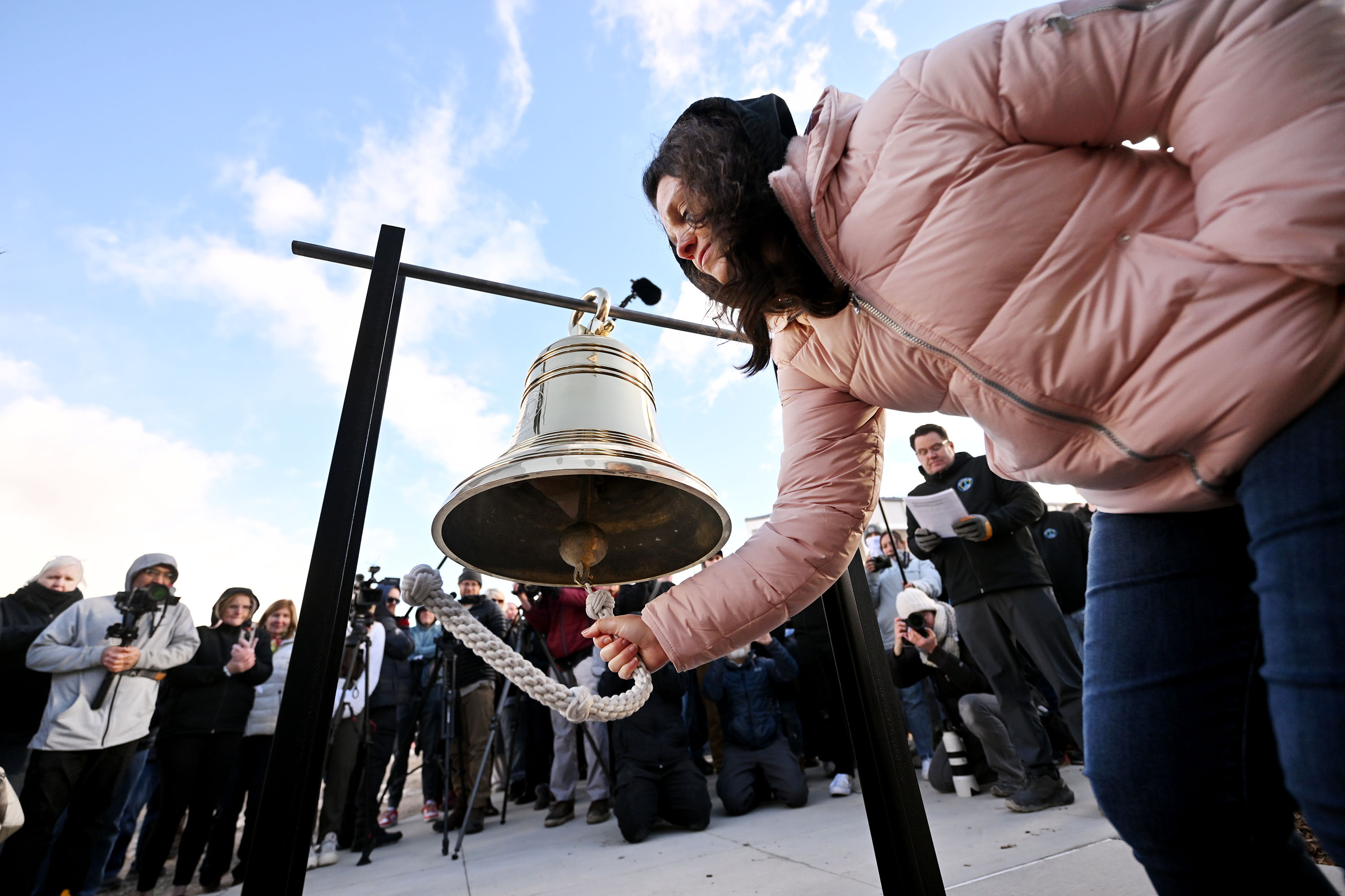 New homeowner Jennifer Davis takes her turn ringing a bell as The Other Side Academy celebrates the grand opening of The Other Side Village on Monday.